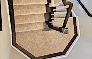 Staircase with beige carpet and dark brown handrails, viewed from above.