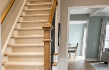 View of a staircase with beige carpet and wooden railing next to a doorway leading into a living room with hardwood floors and dining area.