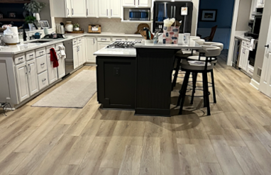 Modern kitchen with white cabinets, black kitchen island, and stainless steel appliances. Vinyl flooring throughout.