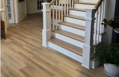 Interior view of a home's staircase with white balusters and light-colored wooden steps, next to a plant in a decorative pot.