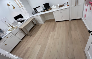 Empty corner of a home office with white cabinets, a desk with two monitors, and light vinyl flooring.