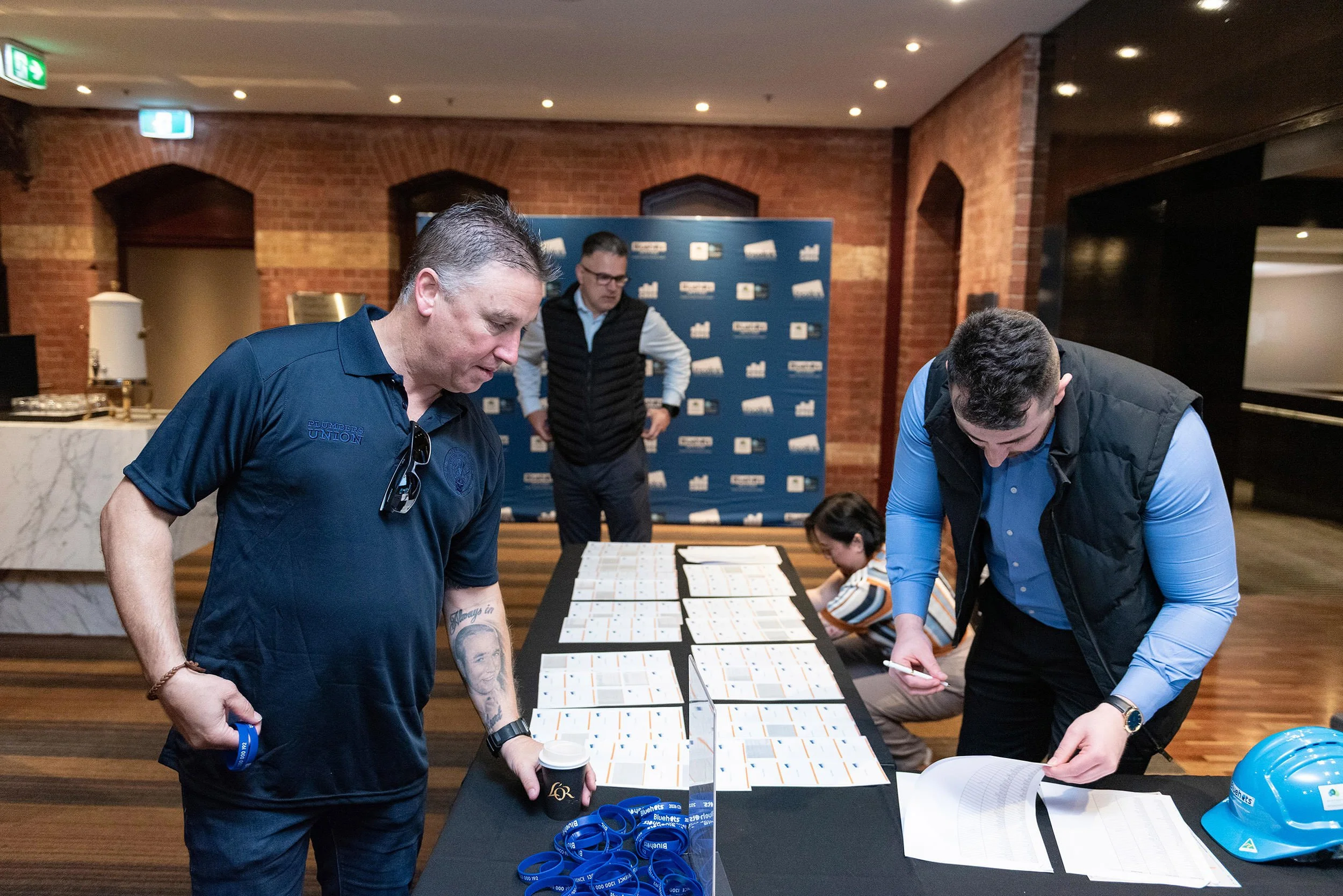 Delegates check in at the Bluehats Conference registration desk, with name badges, blue lanyards and hard hats arranged on the table.