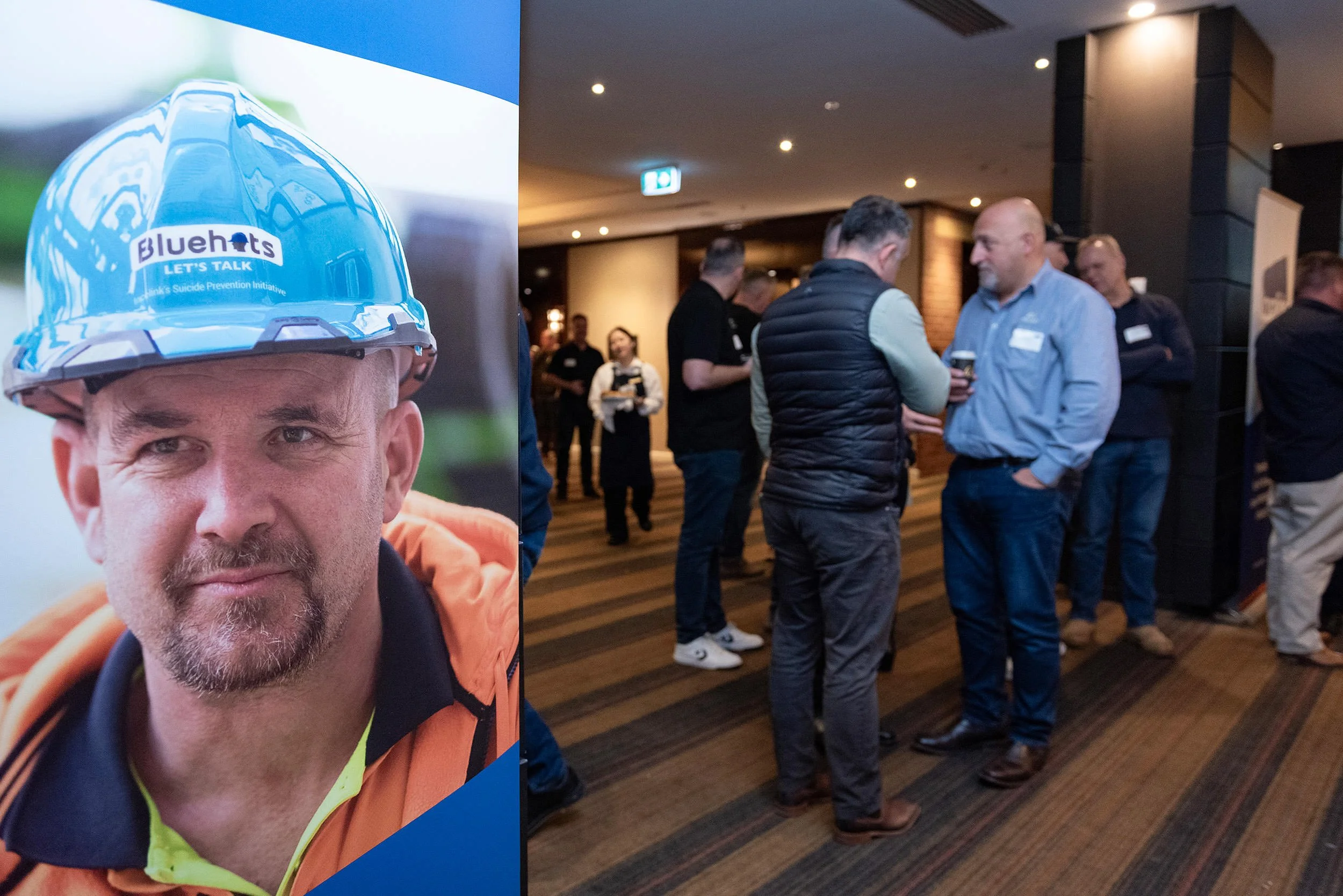 A Bluehats banner featuring a construction worker in a blue hard hat stands beside delegates conversing during a conference break.