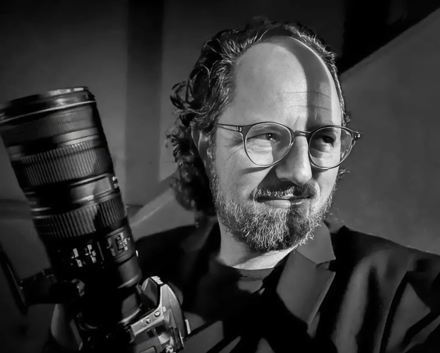 Black-and-white portrait of Hamish John Appleby holding a Nikon camera and telephoto lens.