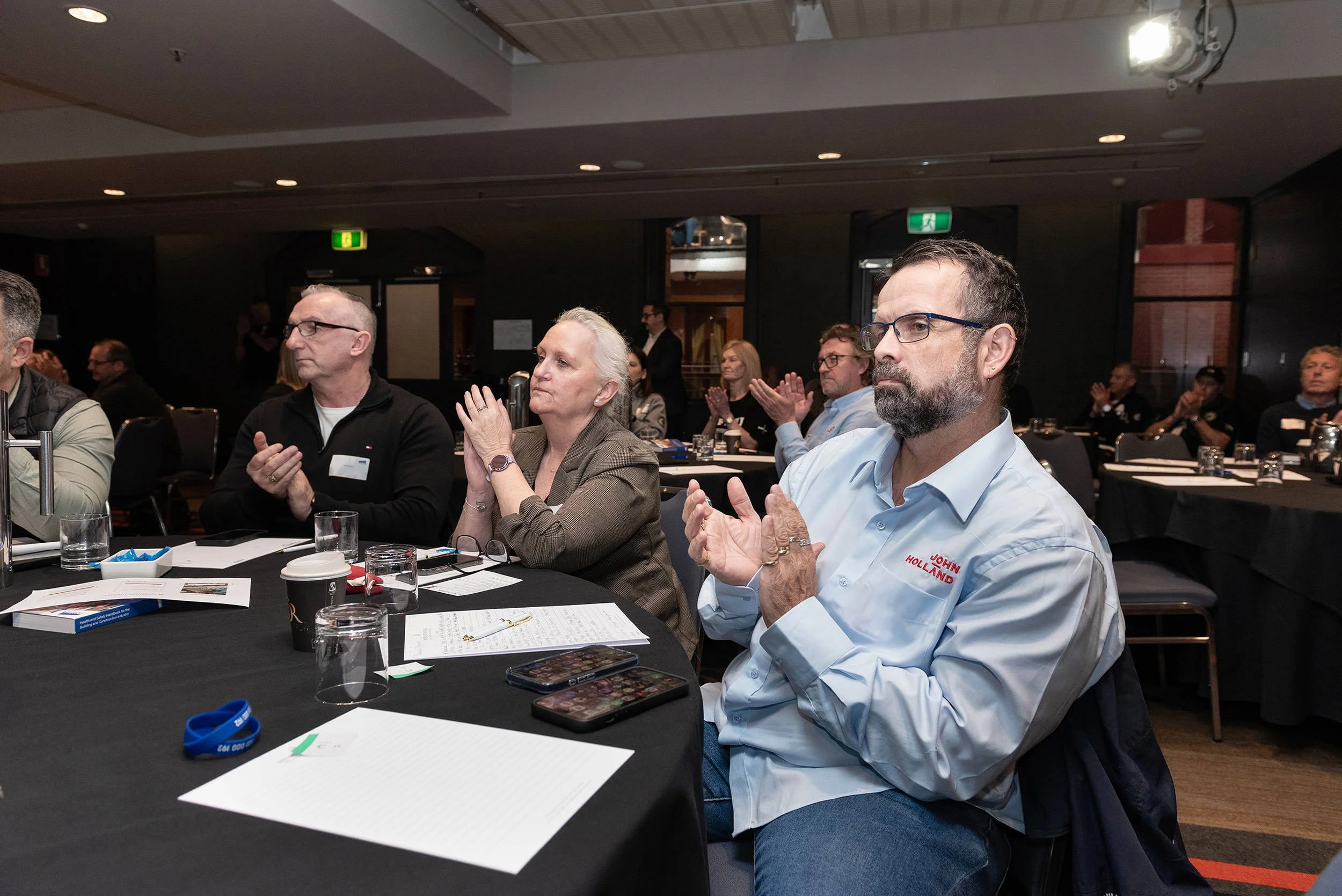 Delegates seated around conference tables applaud during Incolink’s Bluehats Conference in Melbourne.