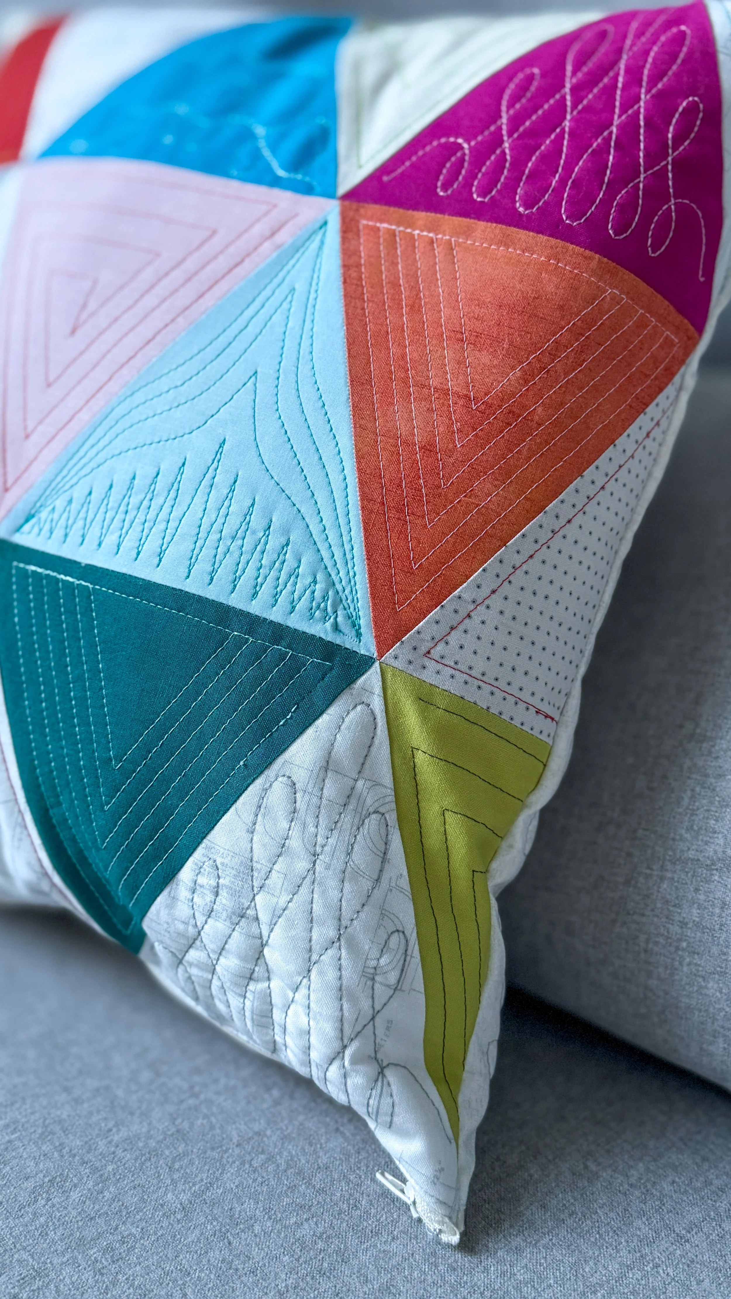 Close-up of looped and geometric stitching on magenta and orange sections of a modern quilted pillow