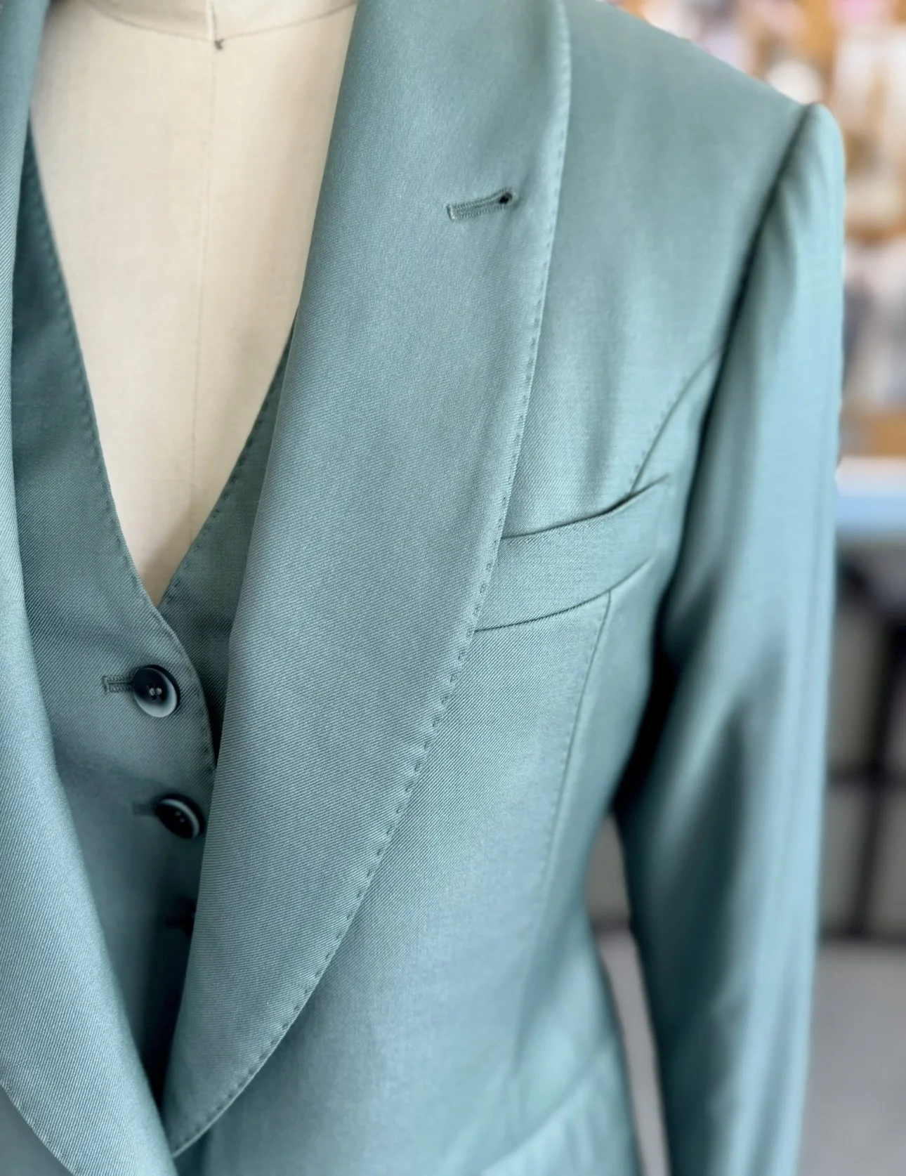 Close-up of hand pick stitching and shawl lapel on bespoke women’s moss green suit jacket, crafted for a Los Angeles. wedding
