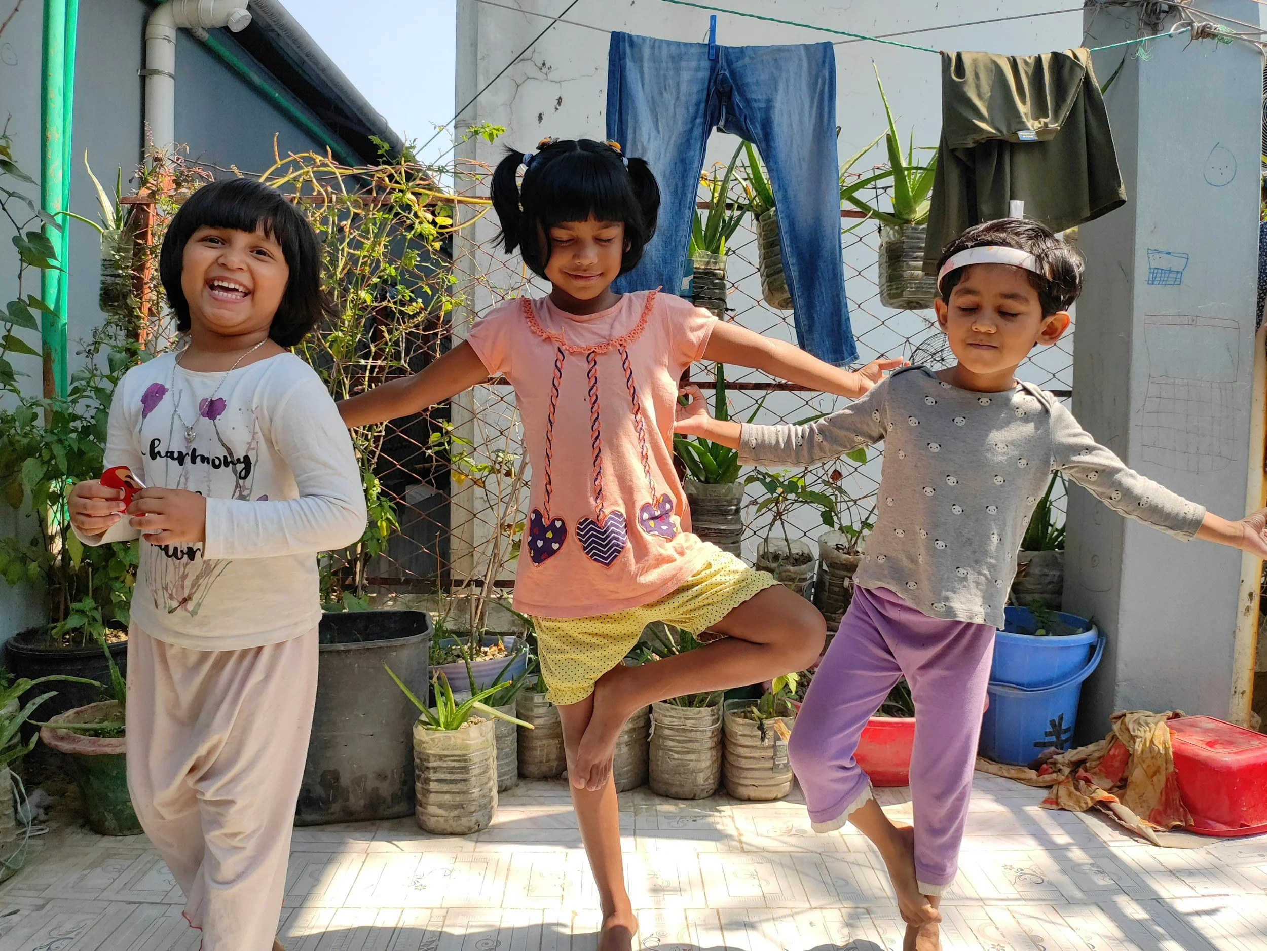 Three children practicing tree pose in yoga, they are smiling and two have their eyes closed.