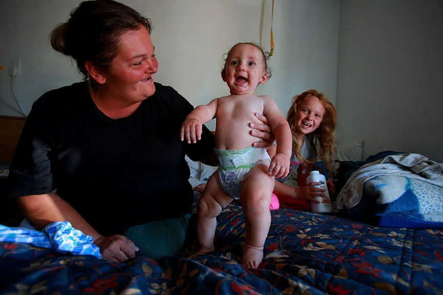 Shannon laughs with her grandson and daughter in a motel she shares with her mother, grandmother and 3 children, after bathing him in the sink.
