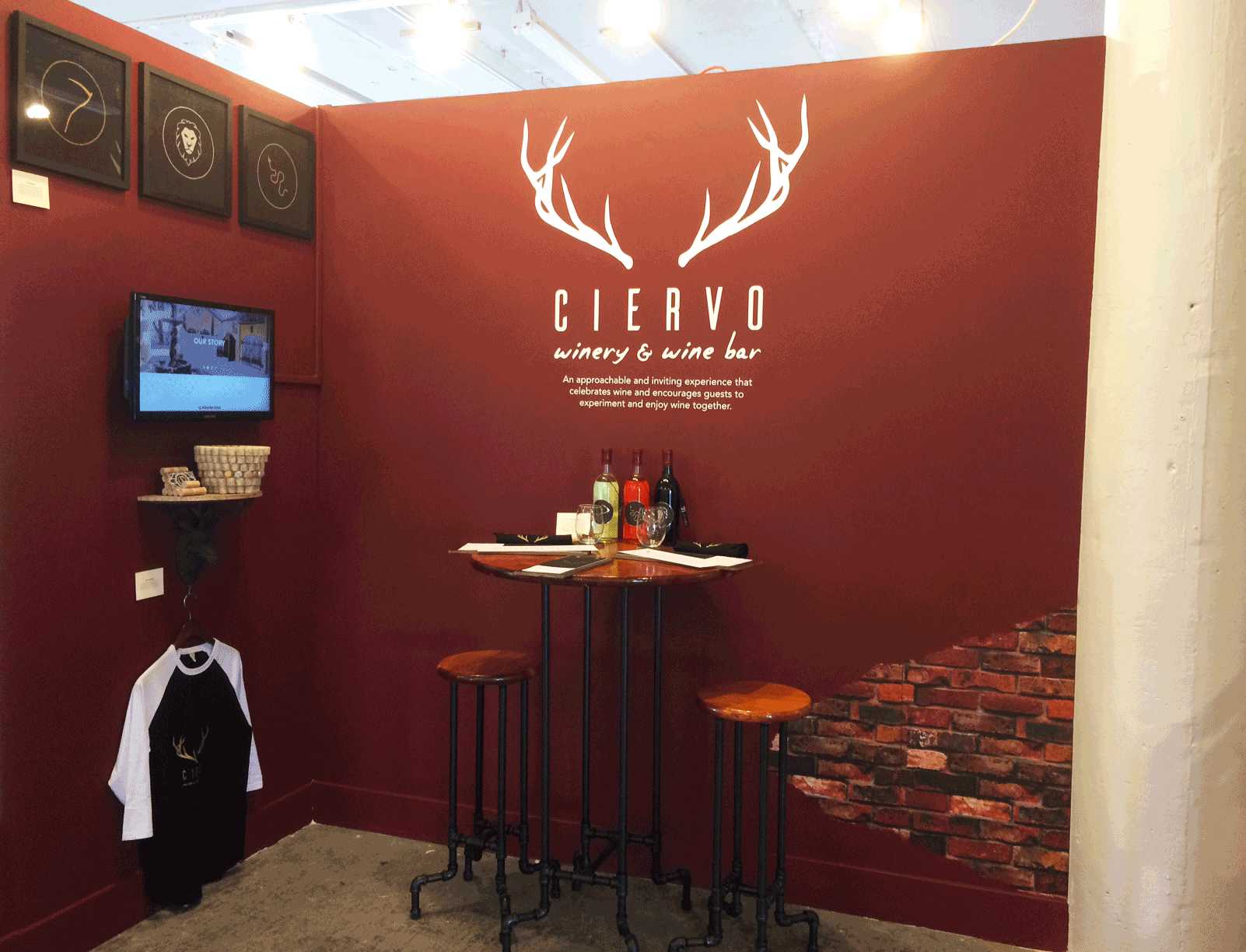 Tradeshow Exhibit Design full of the industrial vibe that the company exudes. Paired with the handmade furniture there is a full table setting with wine packaging examples and the menus. Hanging on the wall, there is a branded baseball tee for emplo