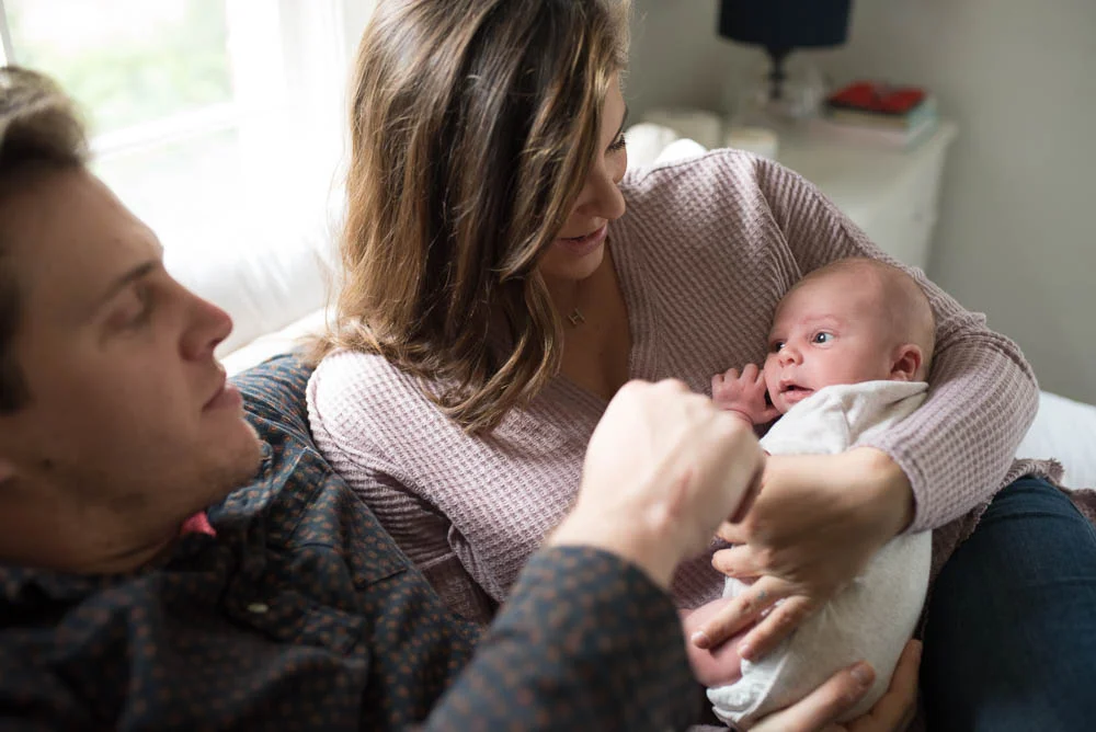 A couple cuddles their newborn baby in their bed during a newborn photography session in Jacksonville, Florida.