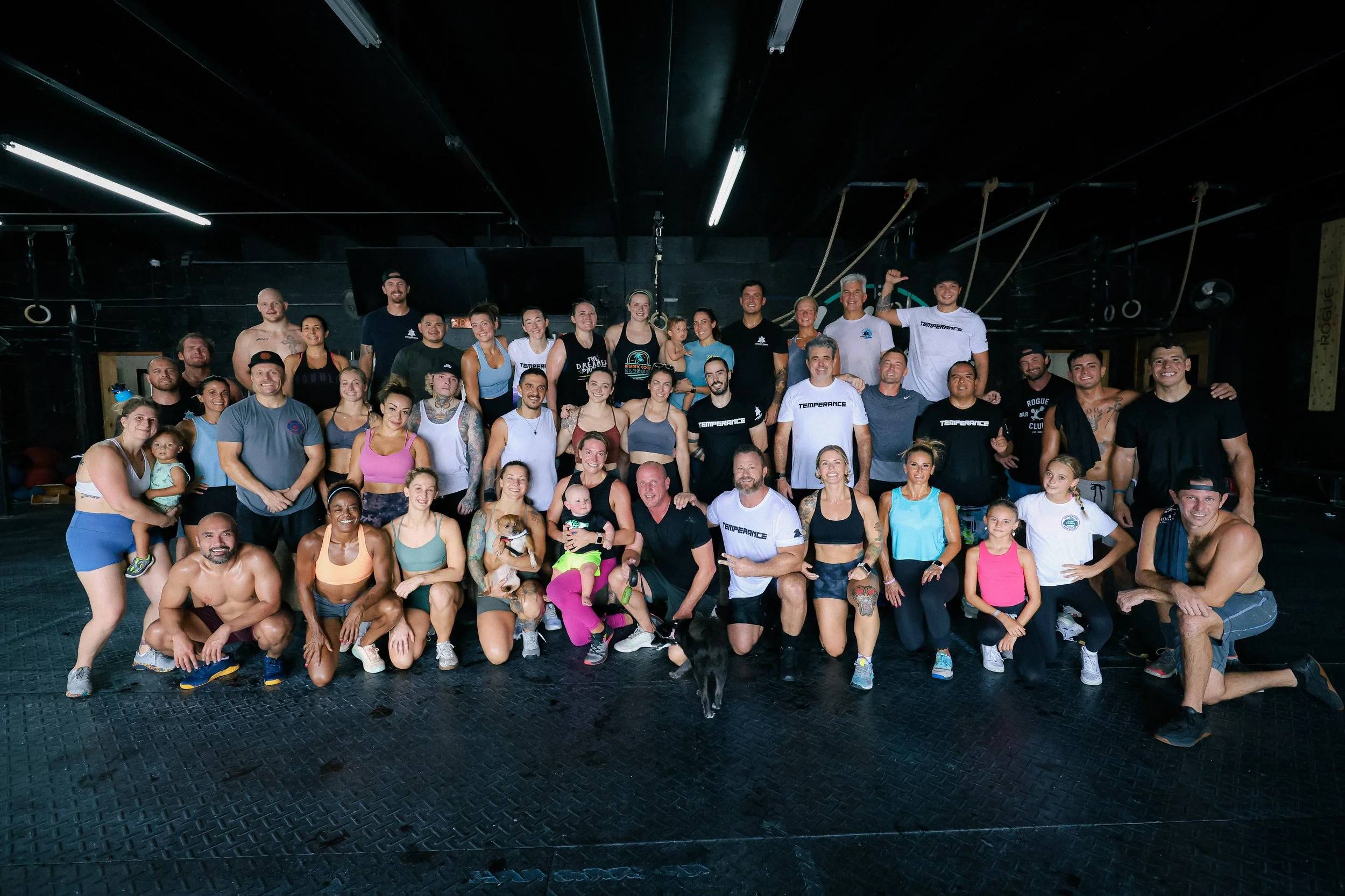 Group of people in a gym, some in workout clothes, posing together after a workout session, diverse in age and ethnicity.