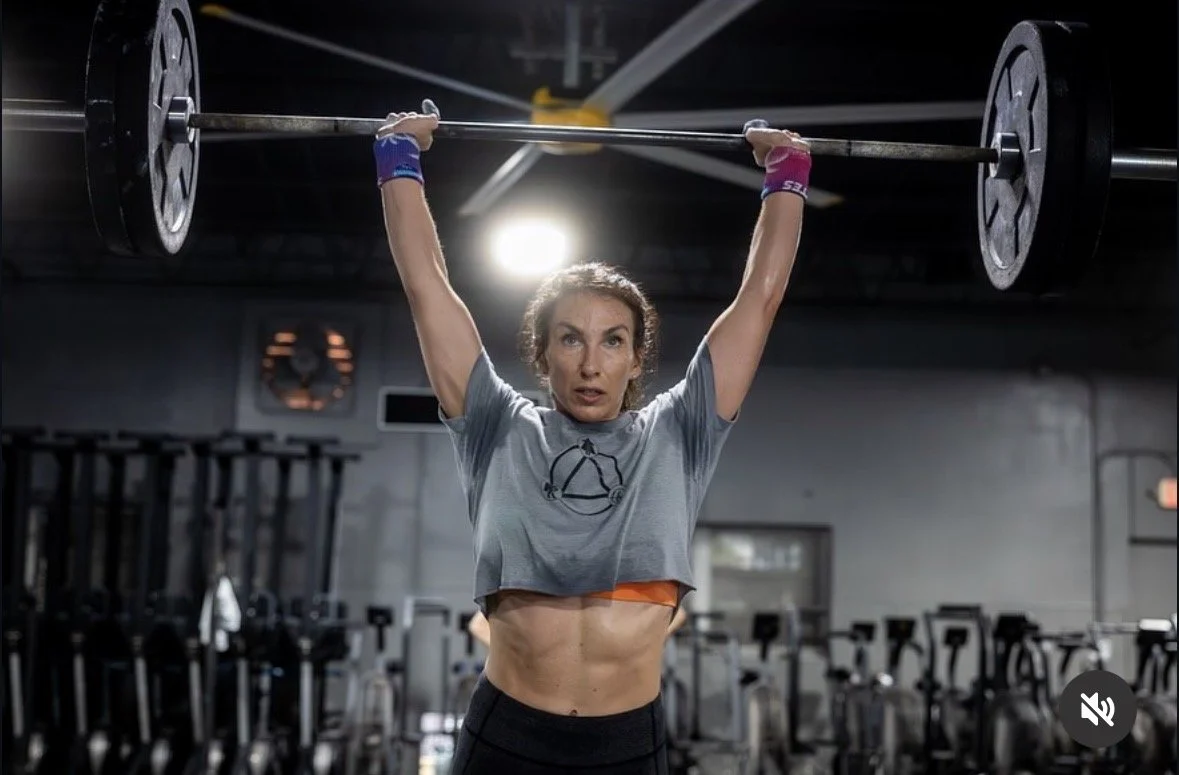 Woman lifting a barbell overhead in a gym.