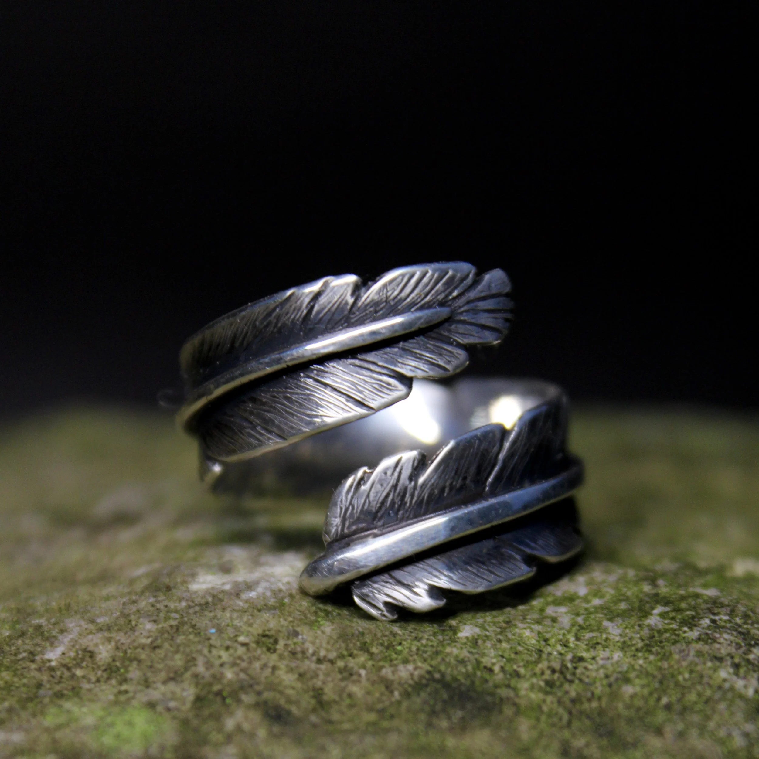 Close-up of a silver ring with detailed engraving, placed on a textured green surface, with a black background.