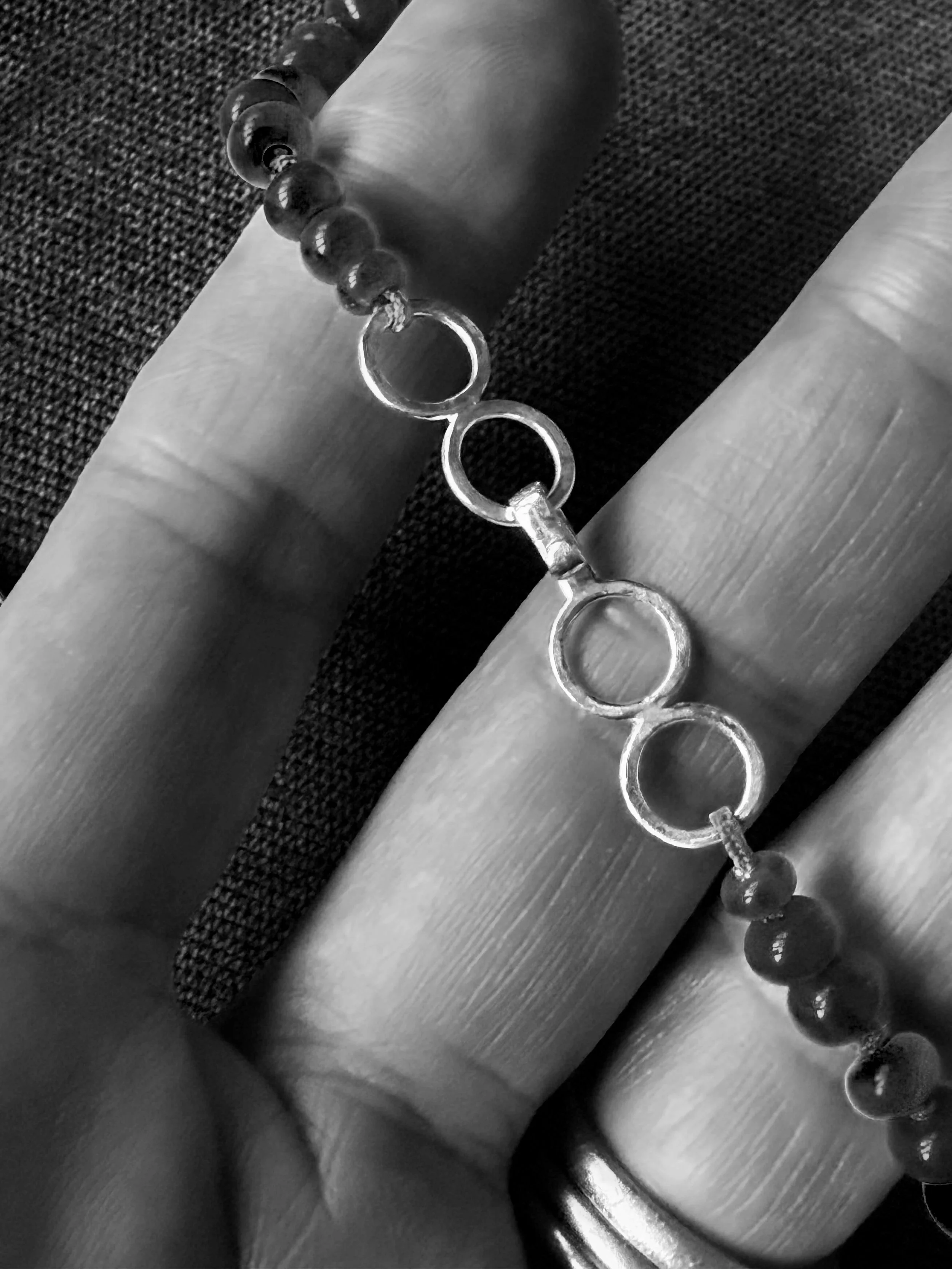 Close-up of a person's hand holding a chain with circular links, resting on a metallic surface with a textured fabric in the background.