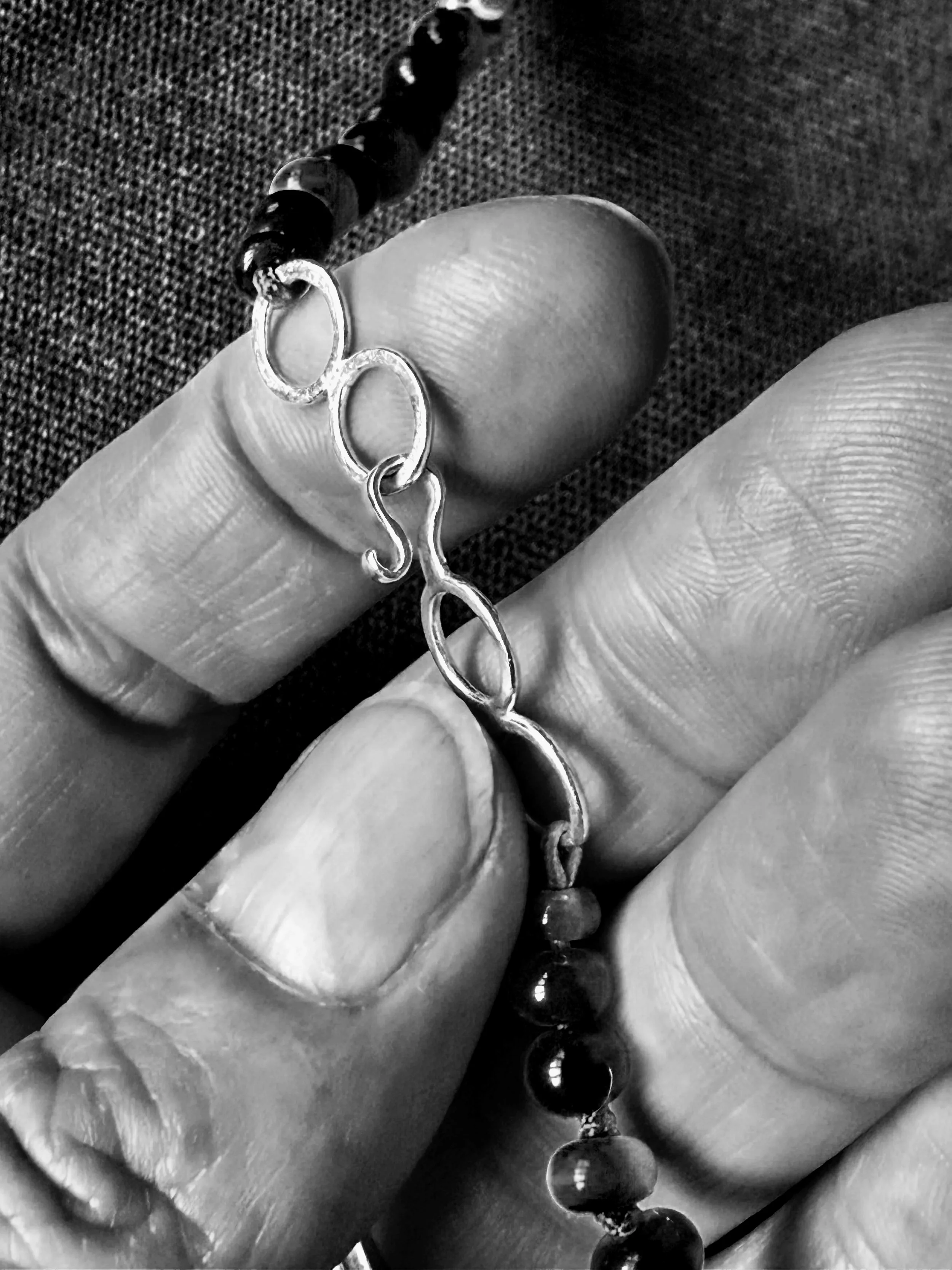 Close-up of a person's hand holding a string of beads with a clasp, with textured fabric in the background.