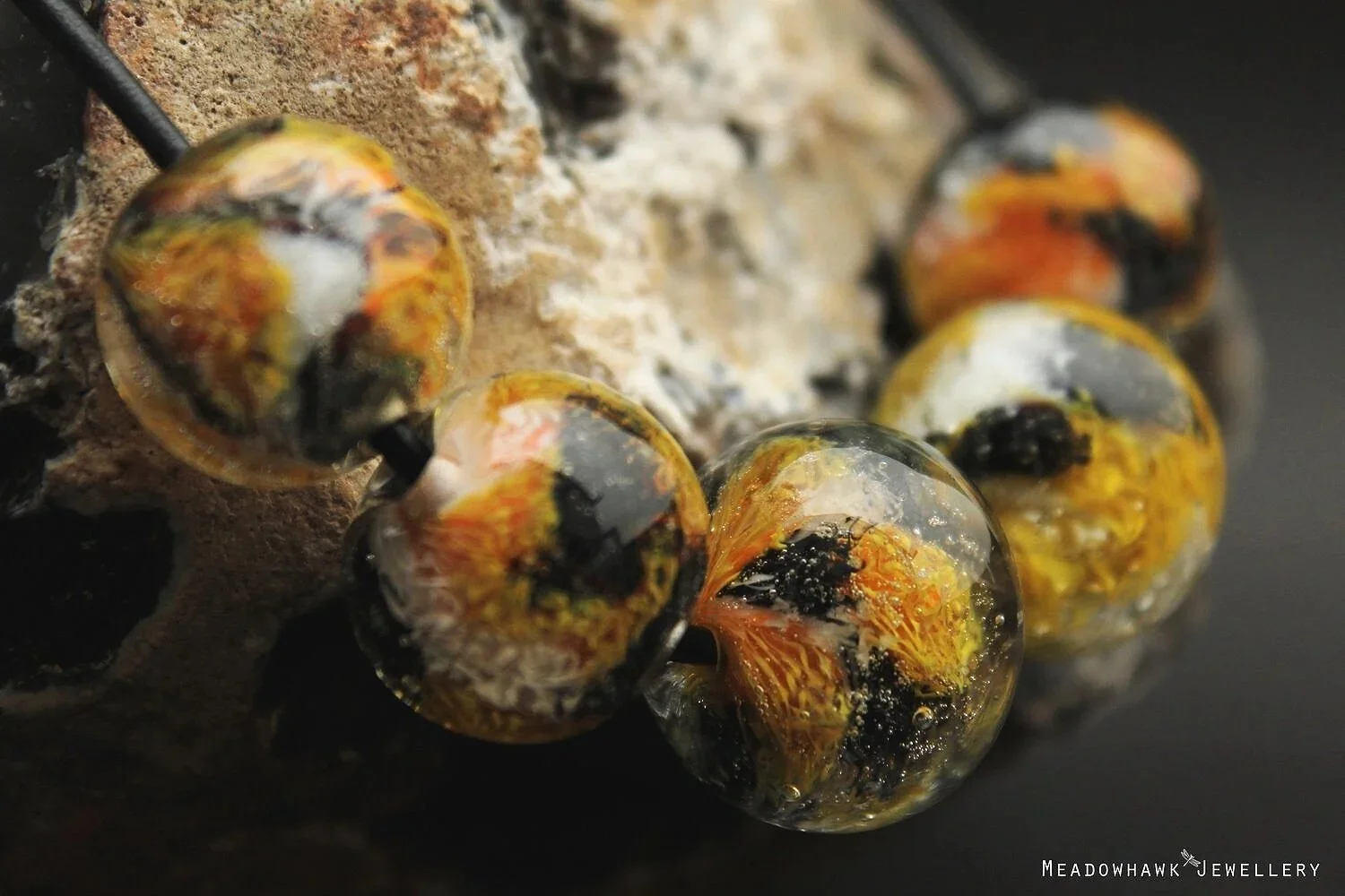 Close-up of colorful glass beads with a marbled pattern, attached to a textured beige and black surface.