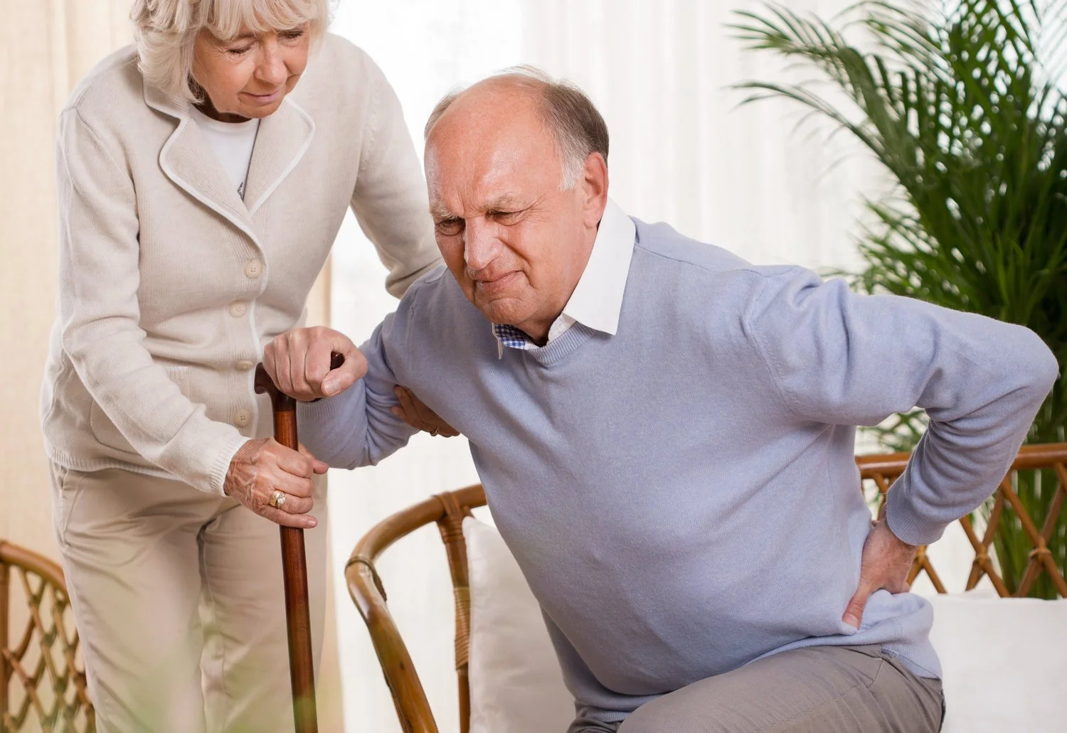Older gentleman with lower back pain and cane, assisted by wife - Disc Disorders Treatment at Sunrise Wellness Center. #BackPainRelief