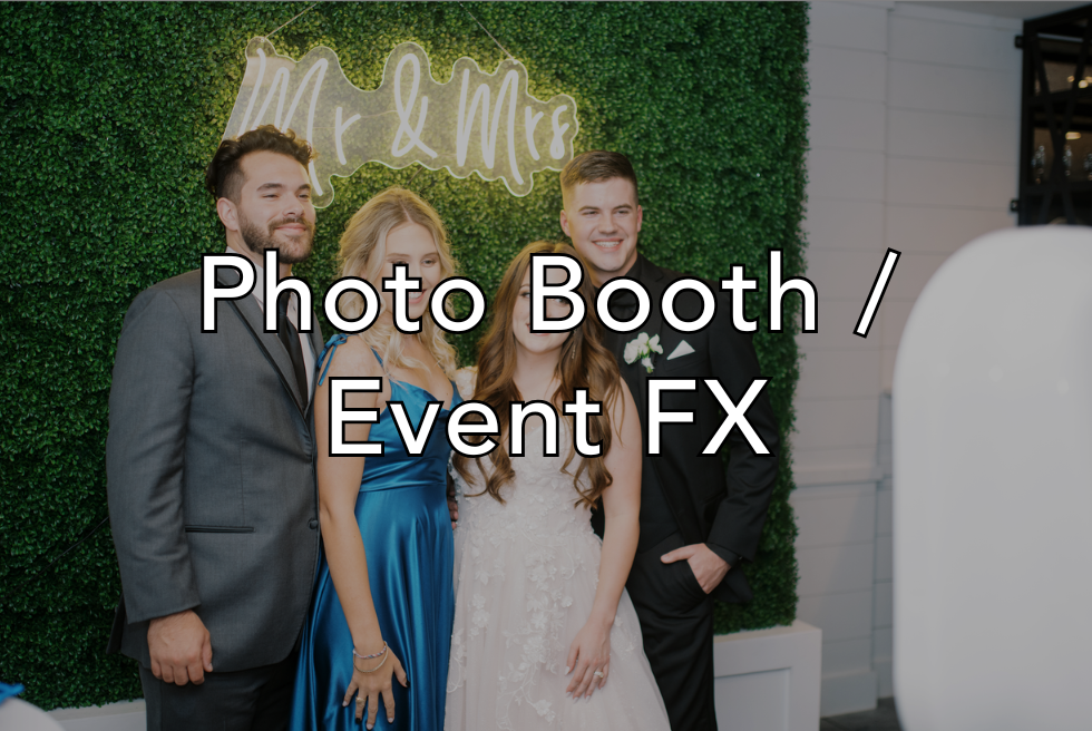 Three people, two men and a woman, standing in front of a green hedge with a "Mr & Mrs" sign, at a wedding photo booth.