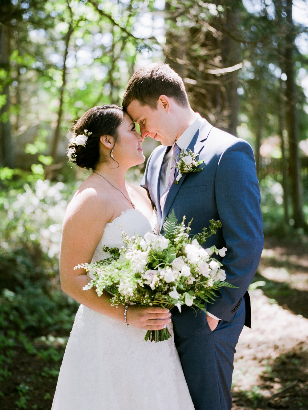  bride and groom nuzzling and holding a white spring themed bouquet 