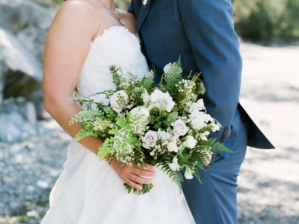  bride and groom nuzzling and holding a white spring themed bouquet 