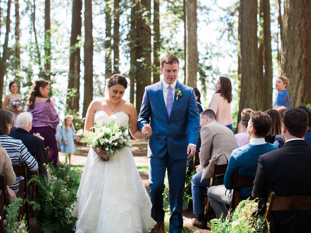  couple walking up the aisle with white spring bouquet in woods 