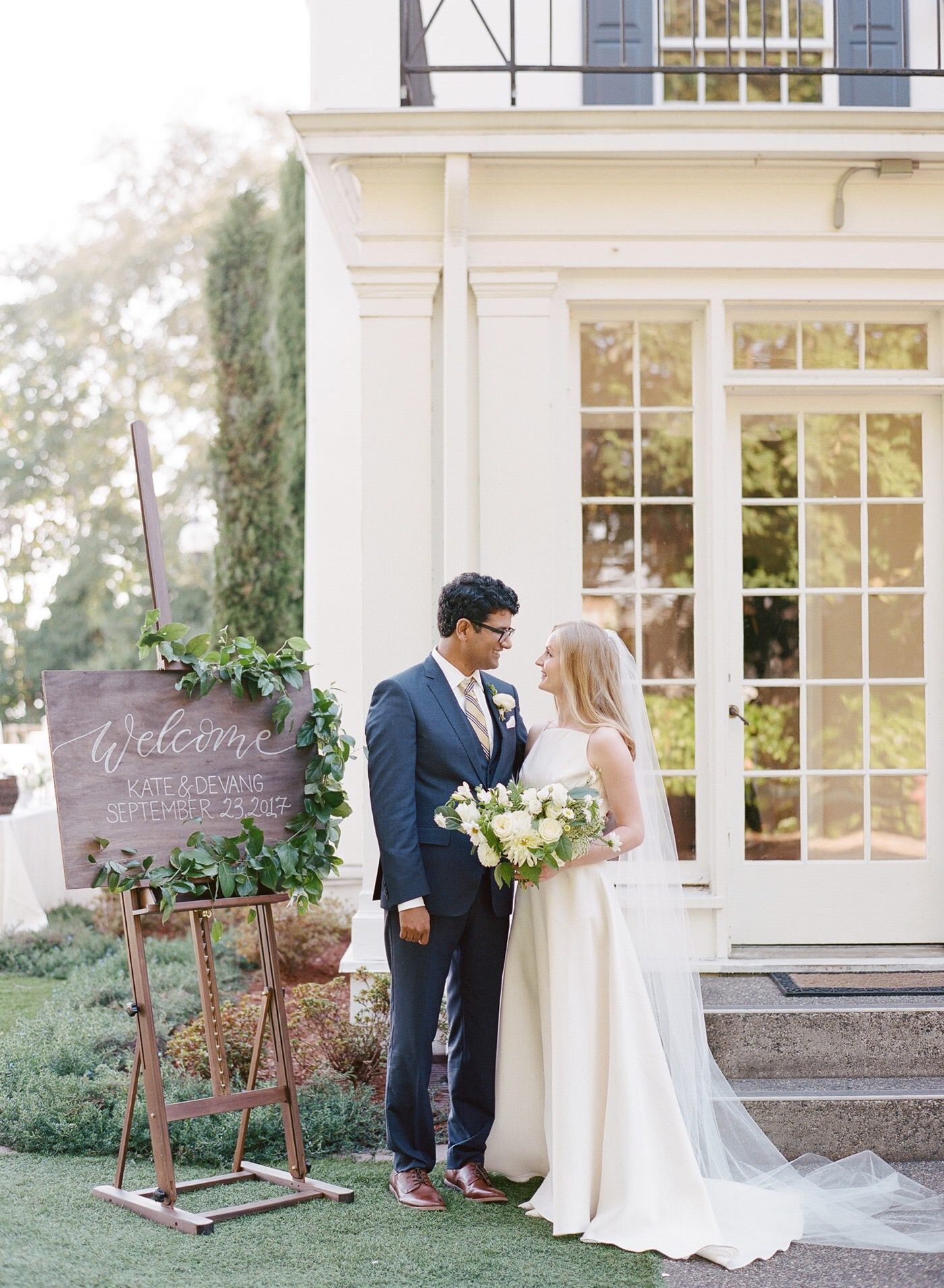 Bride and groom pose next to their welcome sign at The Admiral's House