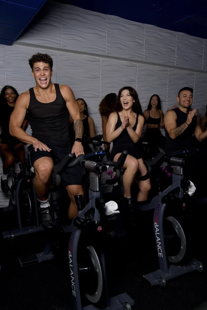 BodyCycle, Honolulu's Rhythm Cycling Studio at Ala Moana Center. With men and women on indoor cycling bikes ready to take a spin class, laughing and clapping.