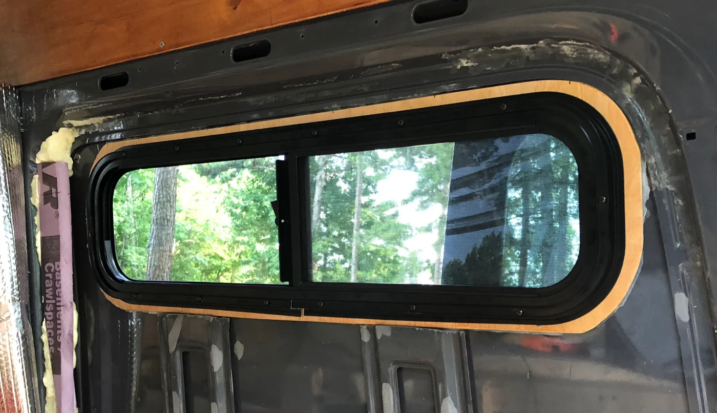 Interior view, showing window clamp ring on our 1/4" plywood spacer. That sucker is on tight. After trimming excess silicone and testing for leaks, we'll cover the area with Thinsulate and reinstall our interior wall.