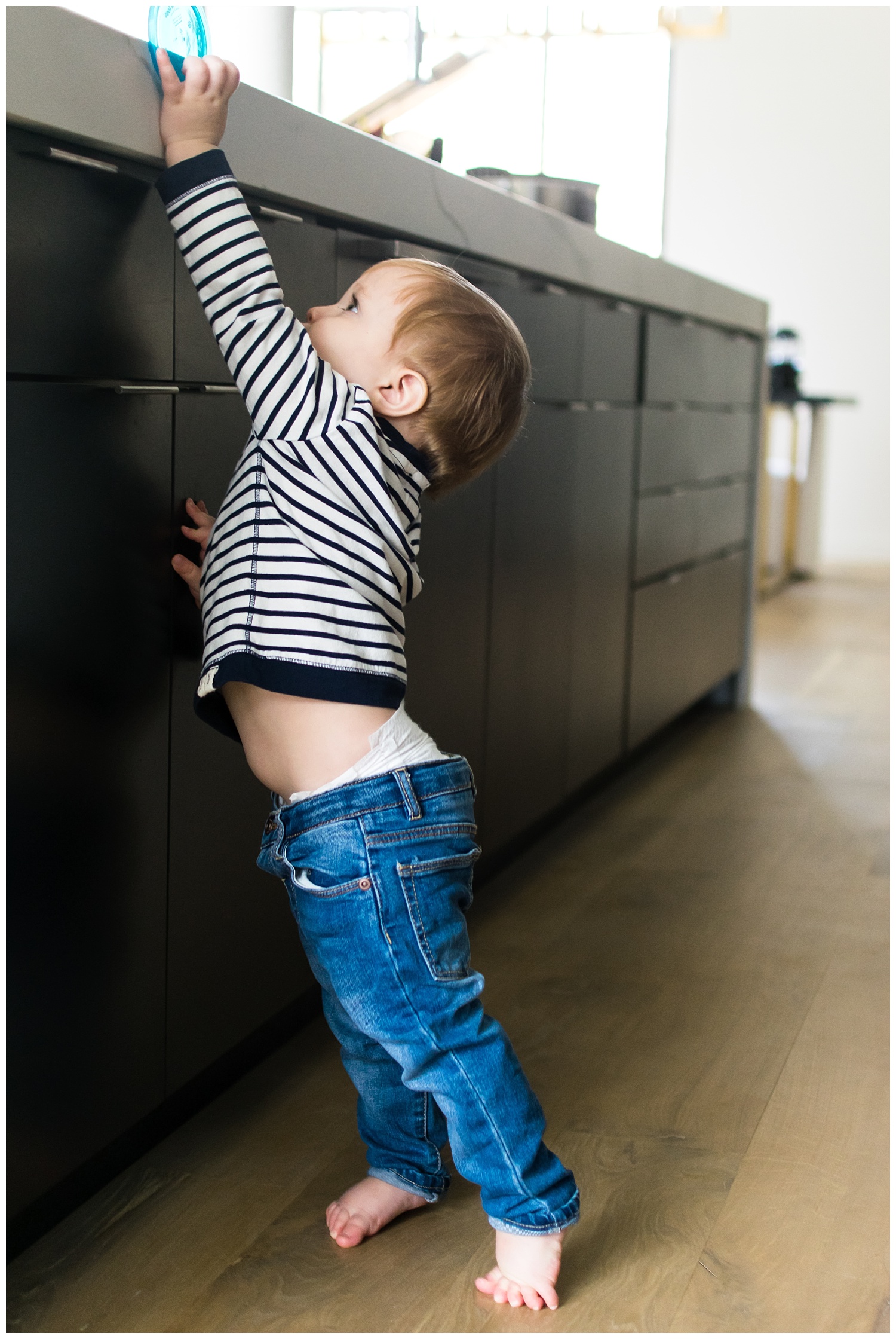 this is an image of a young child standing on his tippy toes trying to reach for his cup. the image was taken during an in home lifestyle session in atlanta georgia.