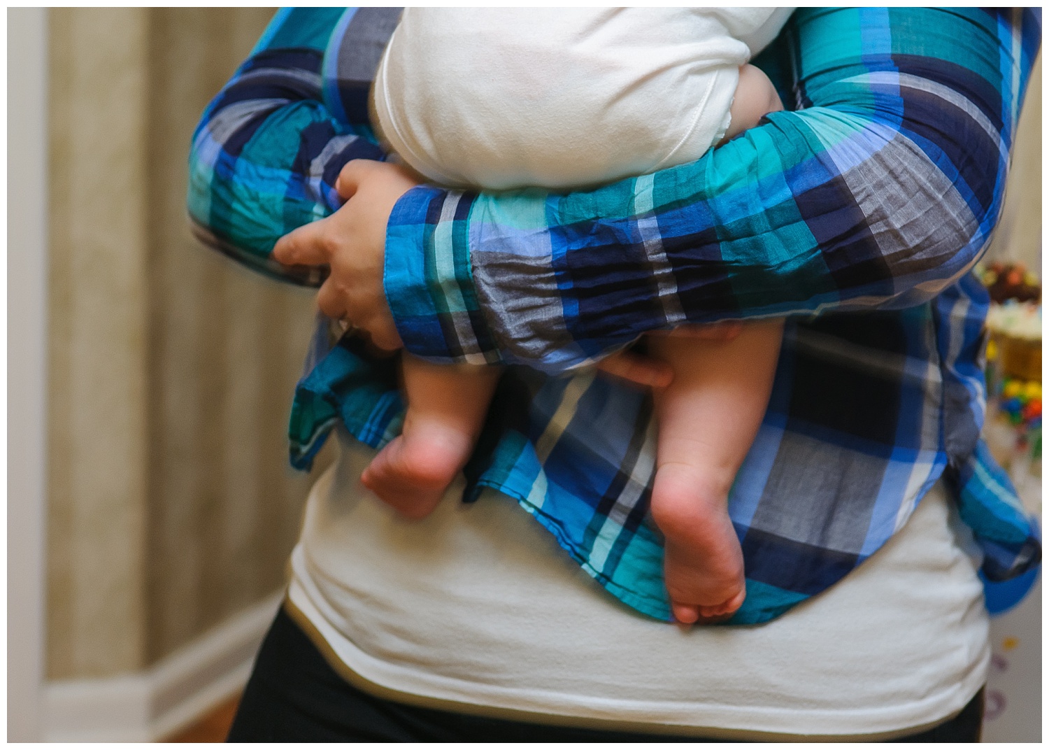 this is an image of the child sitting in mom's arms and the focus is on the way the mom is holding onto the child, with his feet dangling  below.