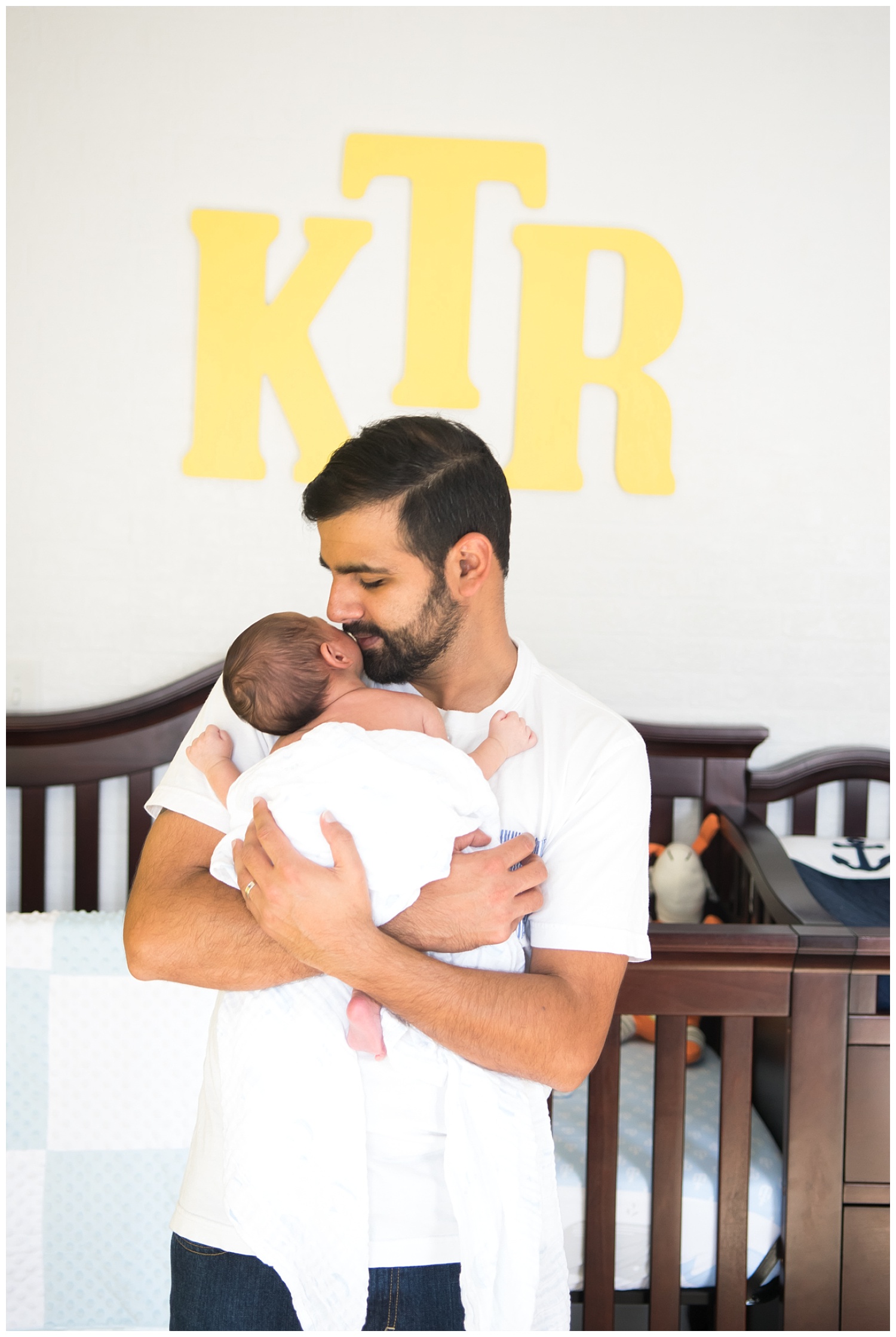 this is an image of a father holding his newborn baby boy and standing in front of the baby's crib. the session took place in decatur georgia