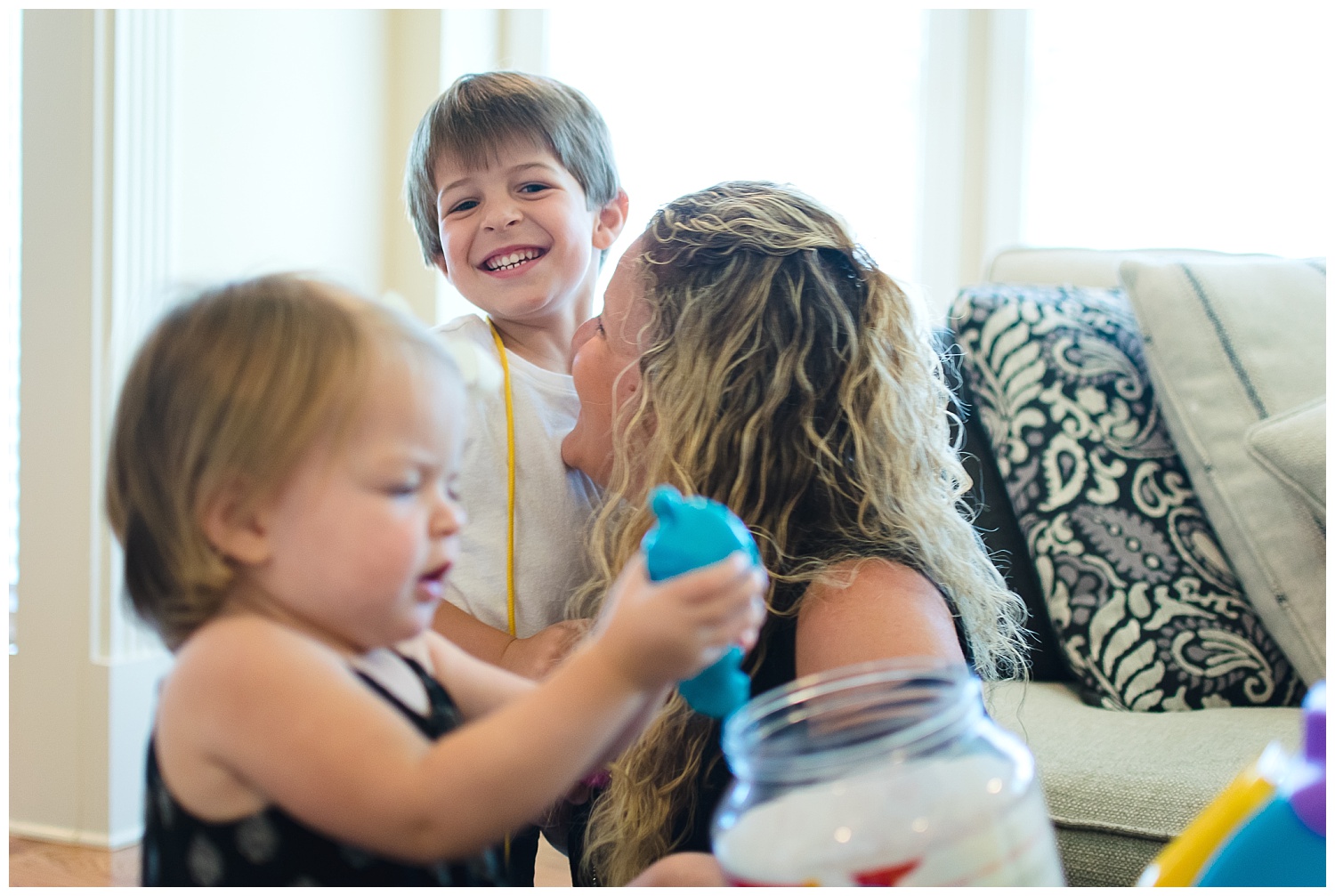 this is an image of a young girl playing with her toys in the foreground and mom playing with another young child in the background in their home