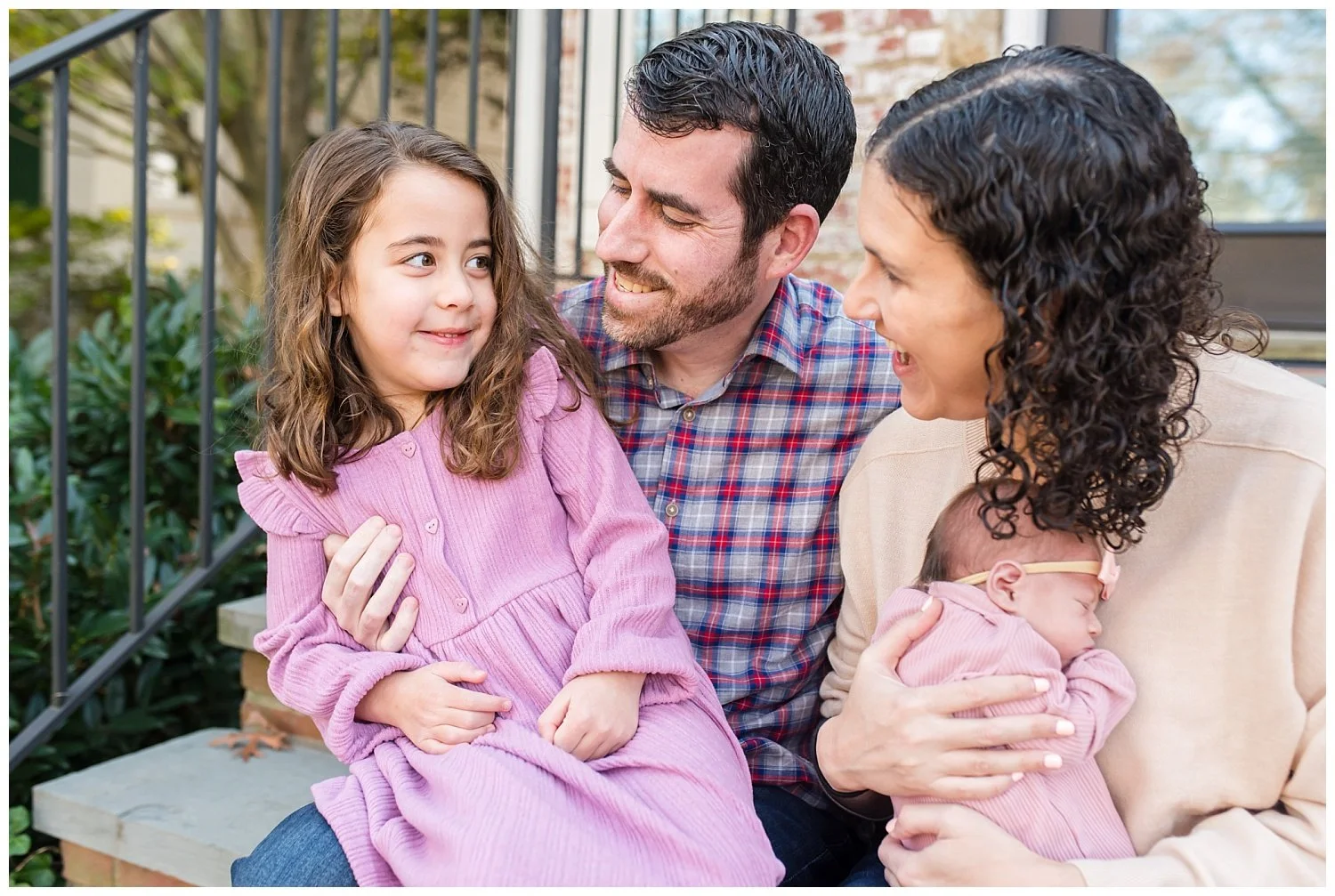 mom, dad, young girl, and newborn baby girl sitting on front door step during Washington DC newborn photography session with Tabitha Maegan