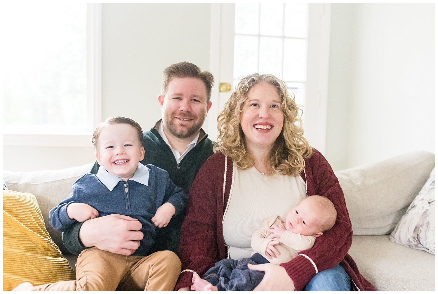 family of four sitting on couch looking at camera at Bethesda newborn photo session with Tabitha Maegan