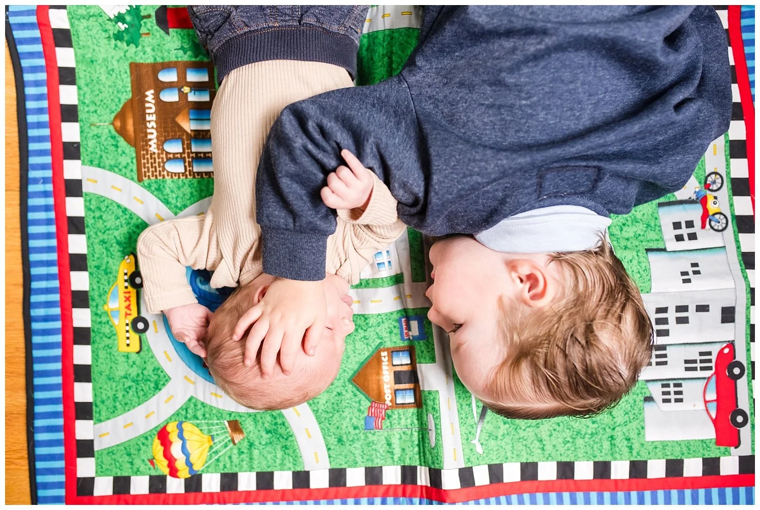 Toddler and newborn baby boy laying on a playmat at Bethesda Maryland newborn photography session with Tabitha Maegan