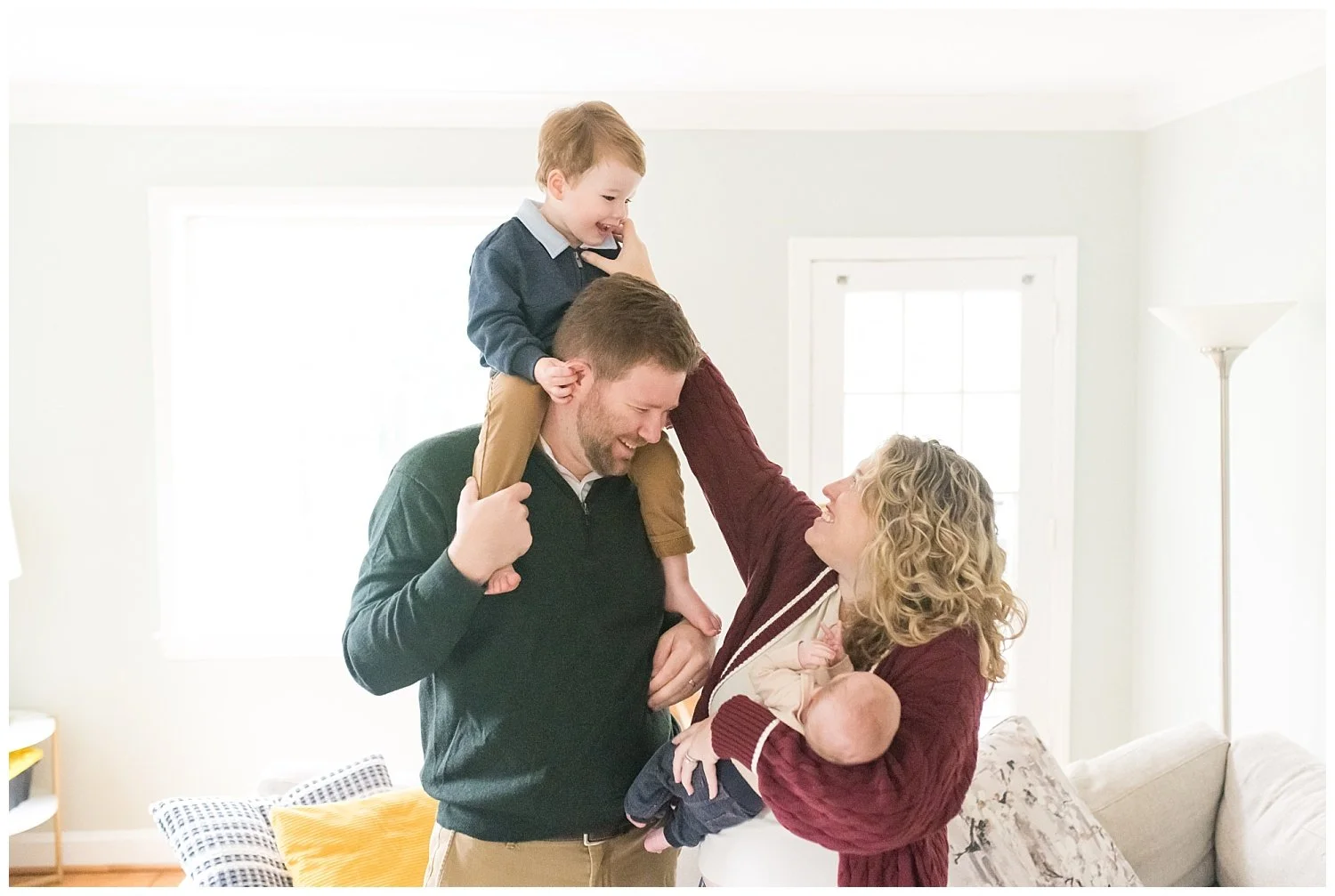 toddler on dad's shoulders while mom holds newborn baby boy and smiles. Taken at Bethesda newborn photo session with Tabitha Maegan