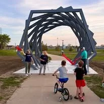 Group of children playing near a large metal arch sculpture in a park on a cloudy day.