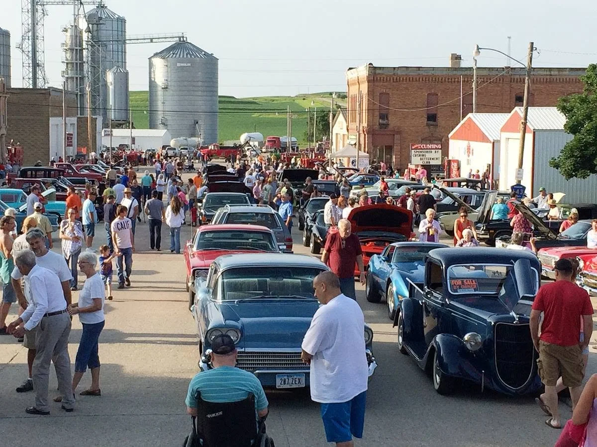 A vintage car show in a small town with many classic cars on display and people walking around.