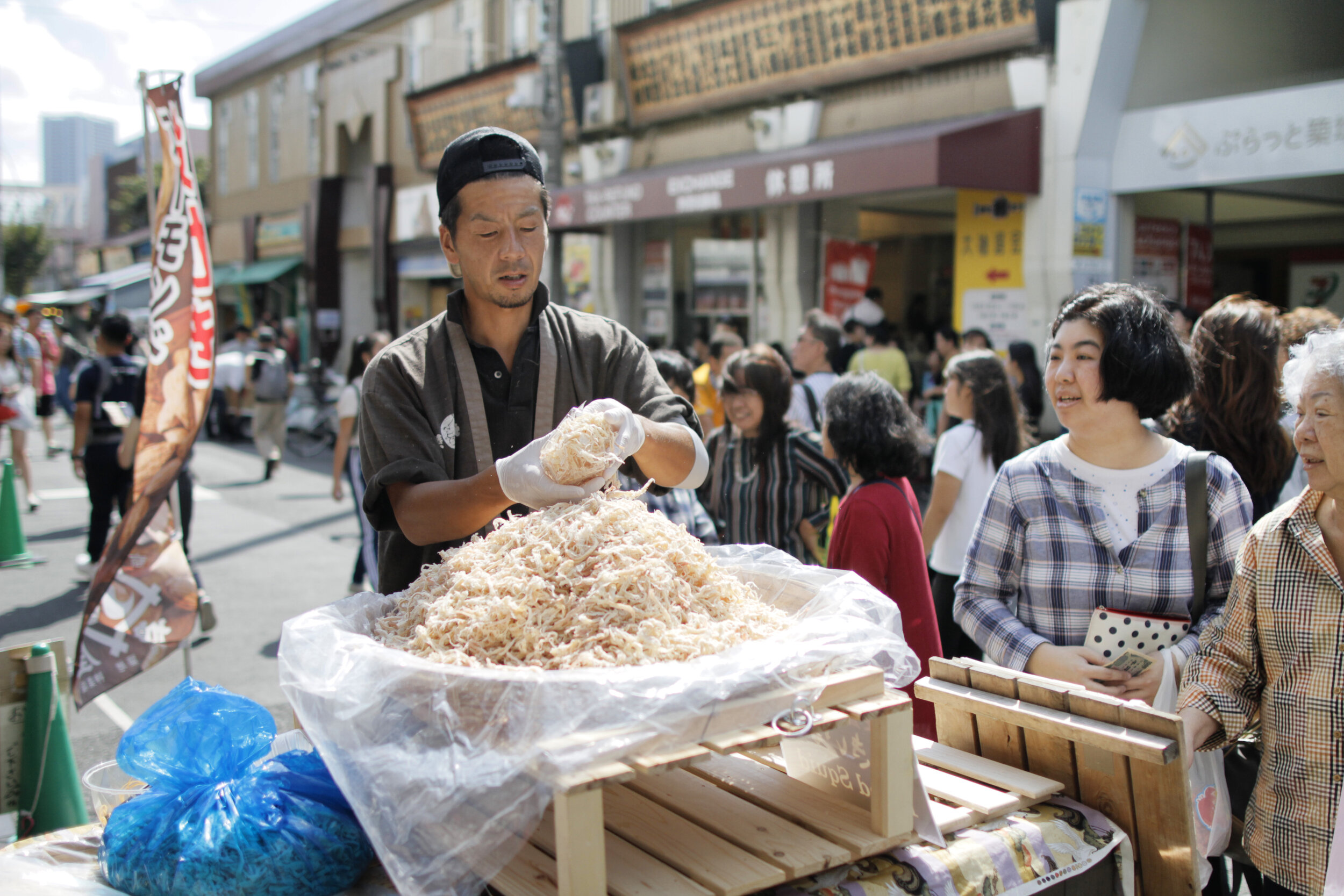 Man preparing dried squid in a busy Japanese market with women watching