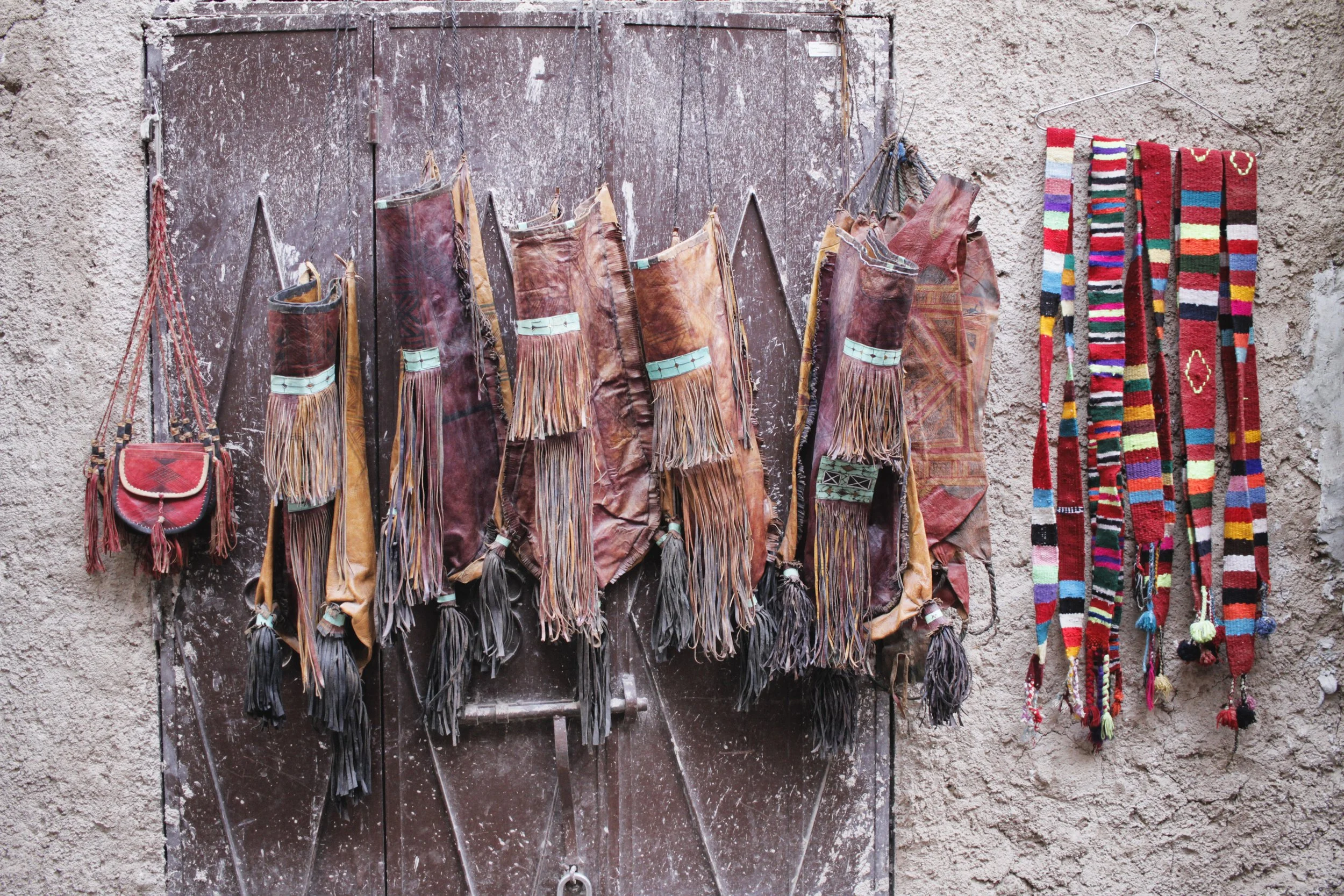 Colorful handwoven textiles and bags hanging on a rustic wall and door. Marrakesh, Morocco.