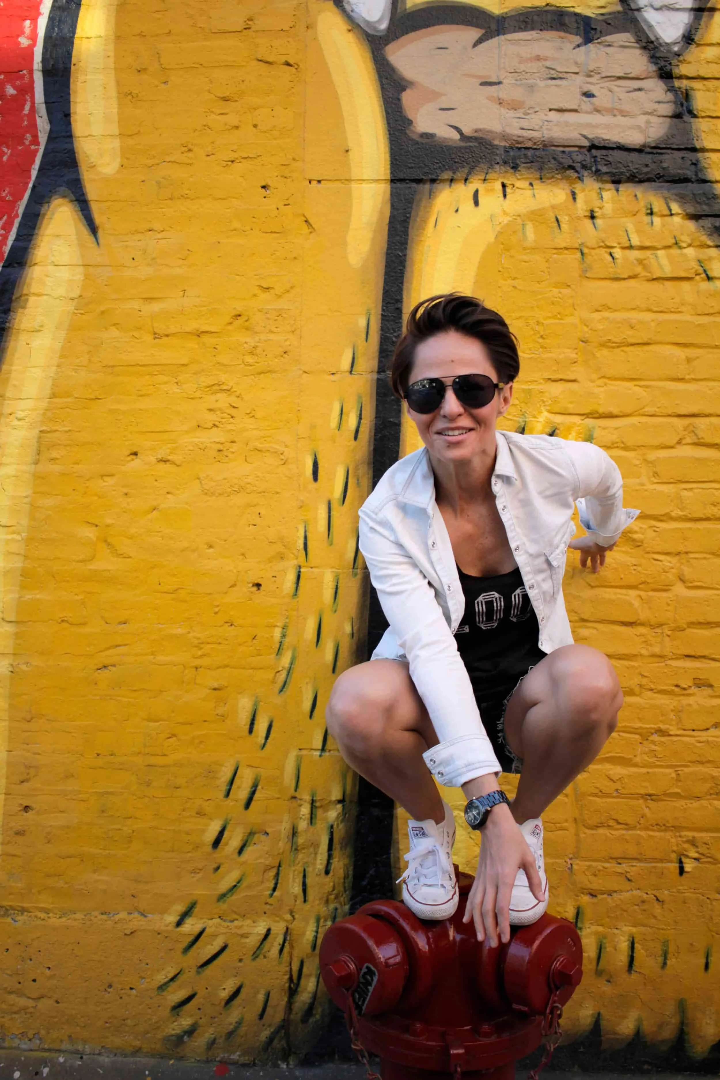 Girl crouched down on a red fire hydrant in from of yellow graffiti wall in Chicago