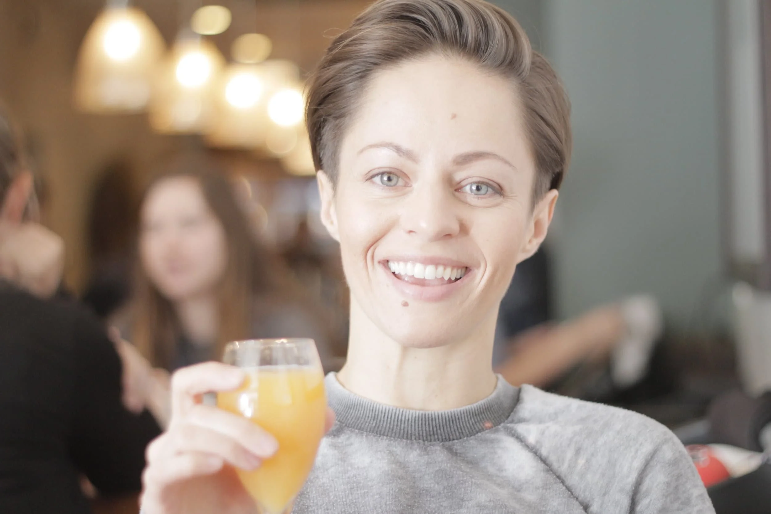 Girl smiling and holding up an orange drink at breakfast