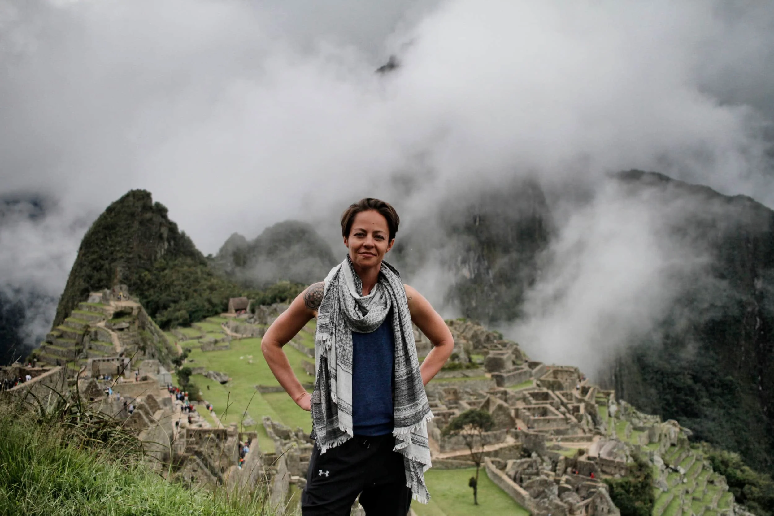 Girl standing above Machu Picchu with ruins and clouds beyond