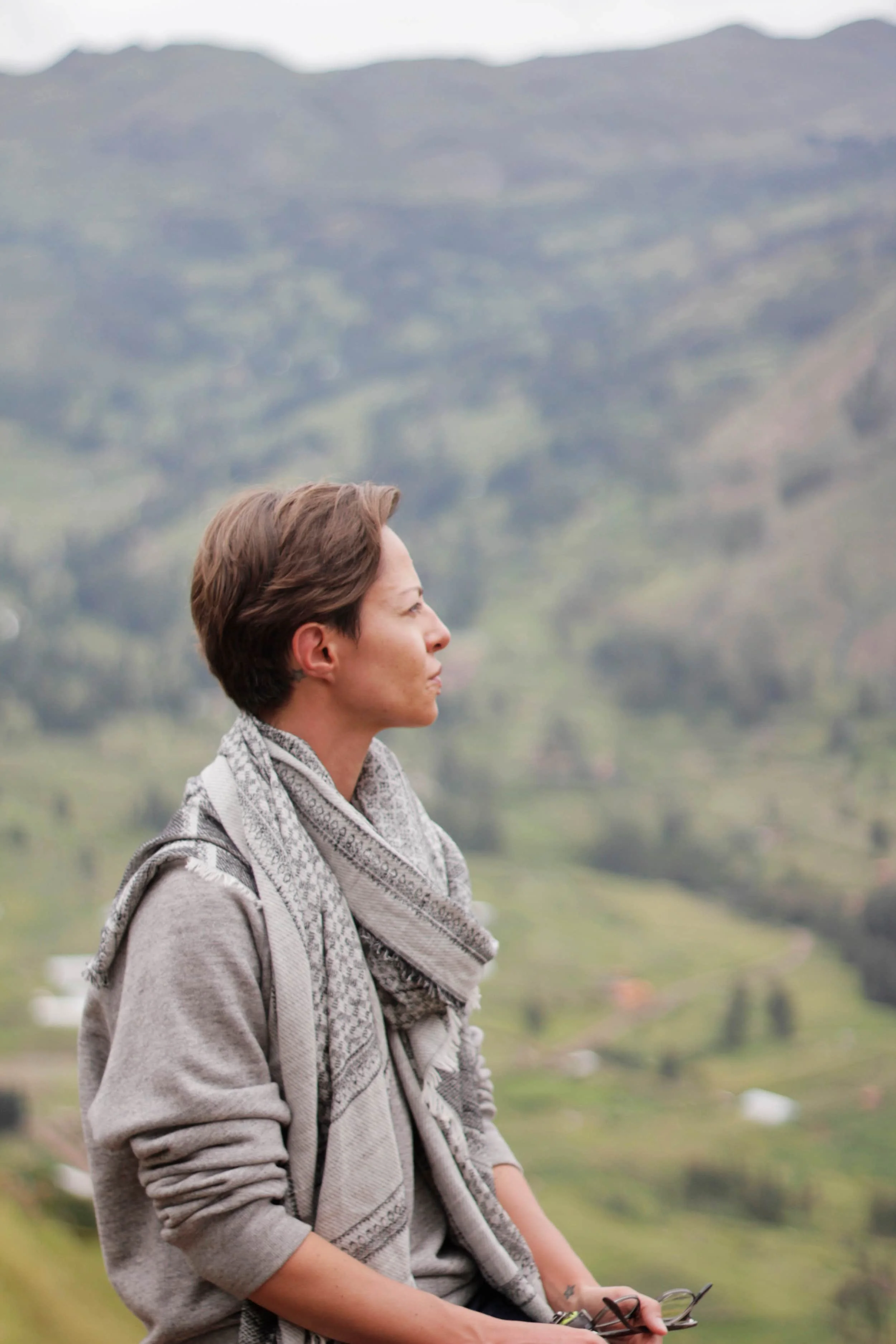 Girl sitting and looking out beyond, landscape behind, in Sacred Valley, Peru