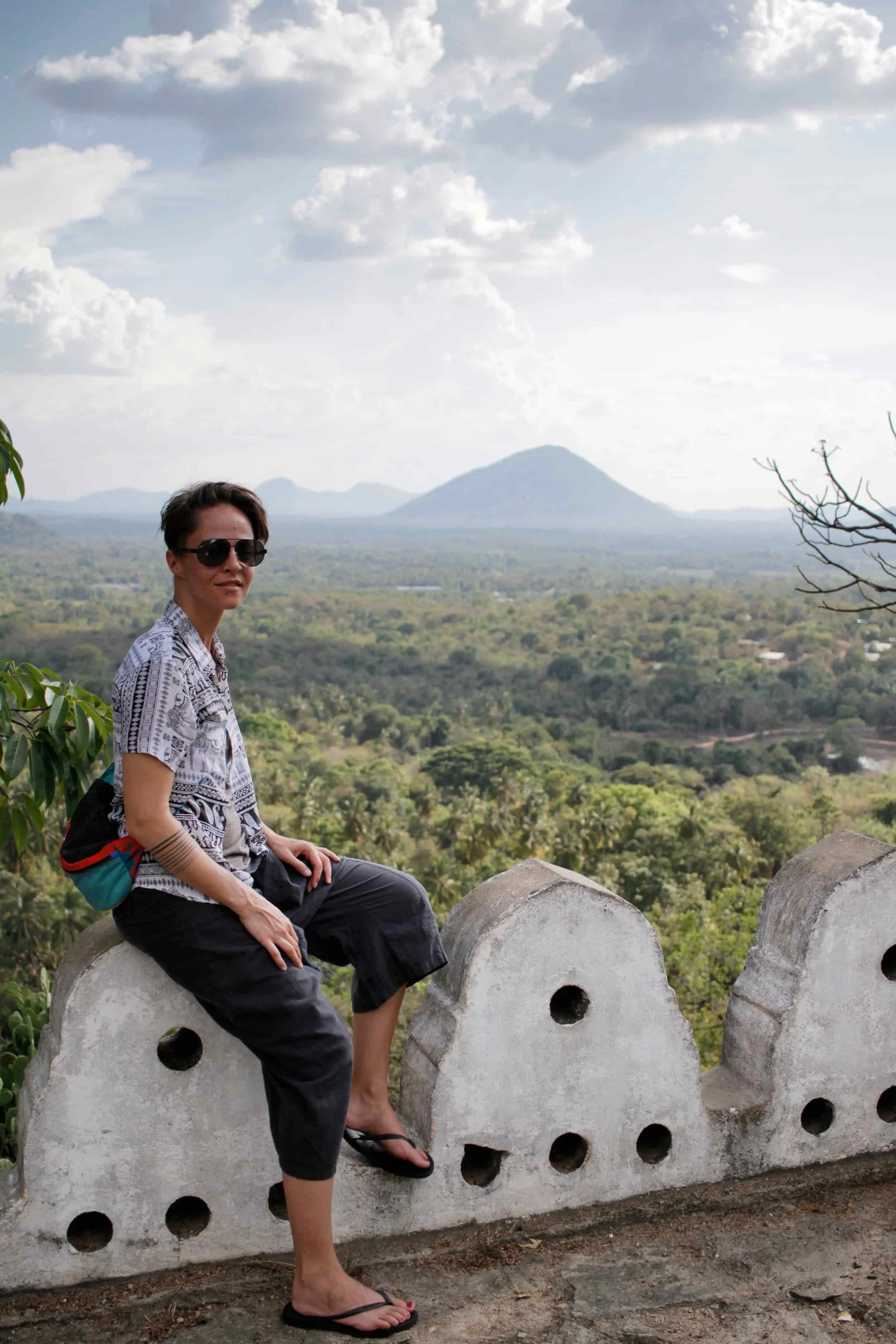 Girl sitting on rounded white stones at edge of a monument overlooking landscape of Sigiriya