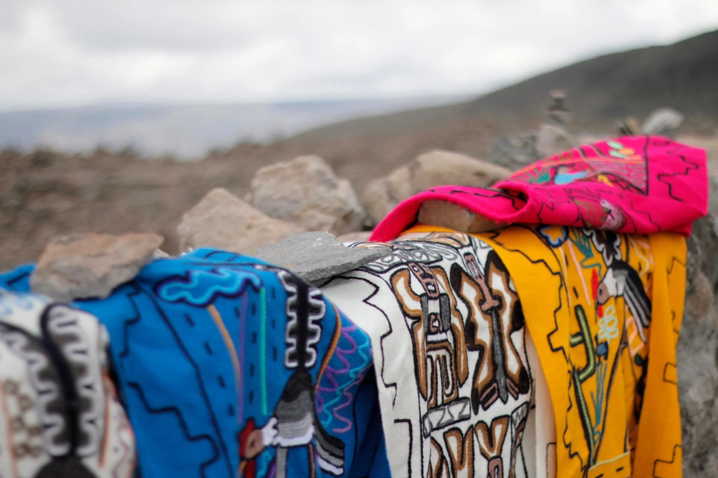 Brightly colored textiles for sale placed over a stone wall