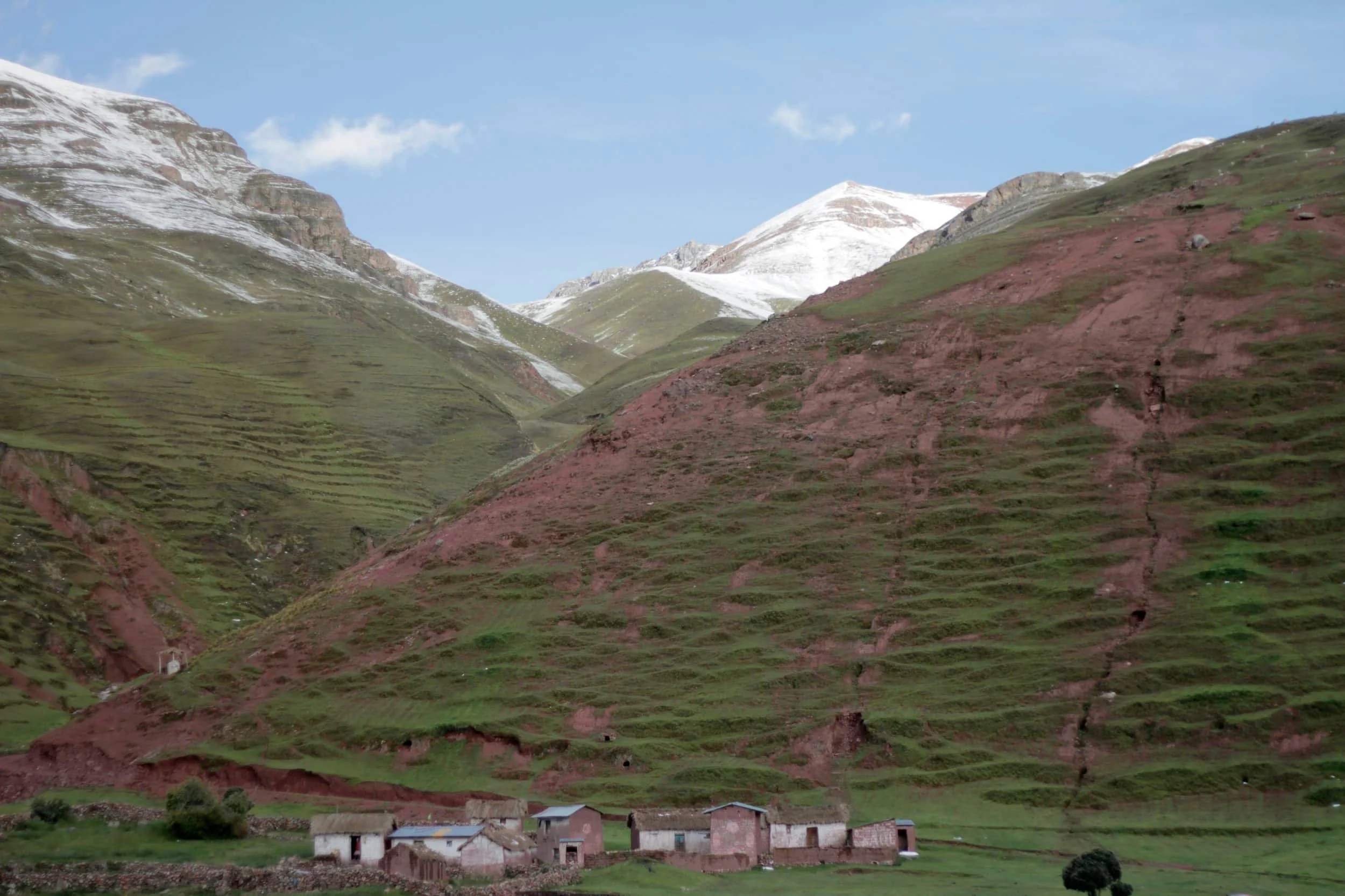 Massive green mountains with snow on the top and a tiny village below in Peru