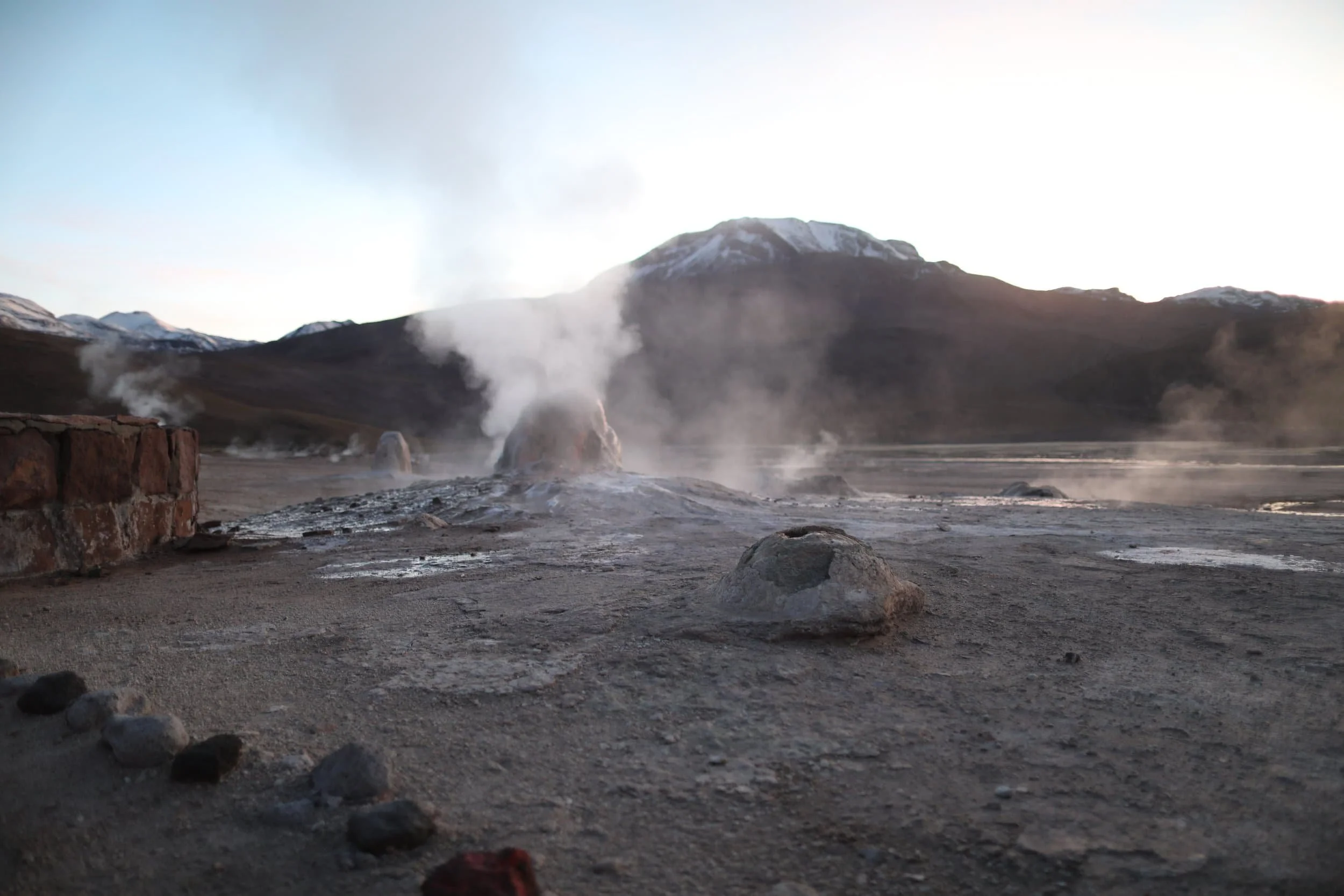 Steam rising from the El Tatio Geysers at sunrise, surrounded by the dramatic volcanic landscape of the Atacama Desert in northern Chile.