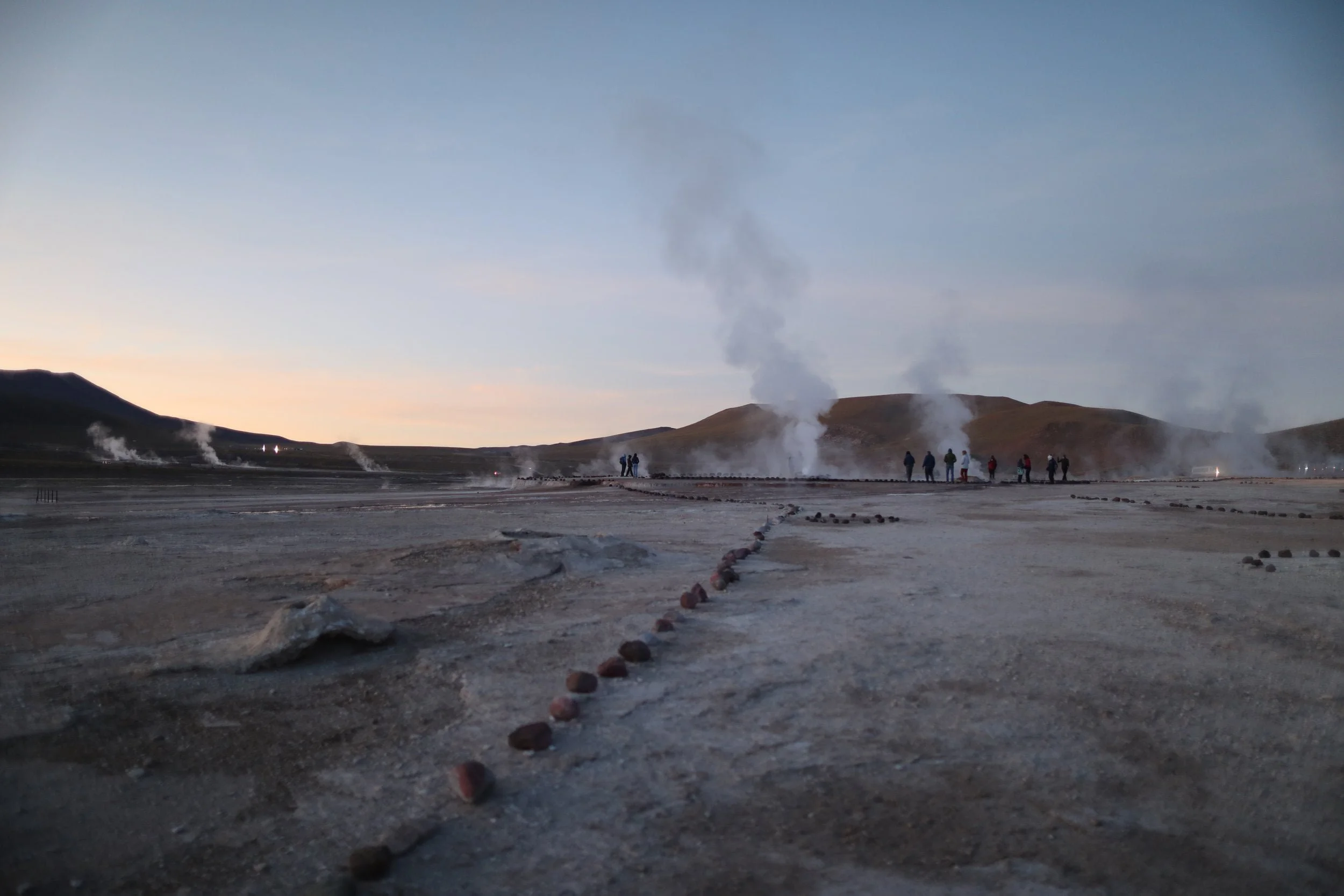 Steam rising from the El Tatio Geysers at sunrise, surrounded by the dramatic volcanic landscape of the Atacama Desert in northern Chile.